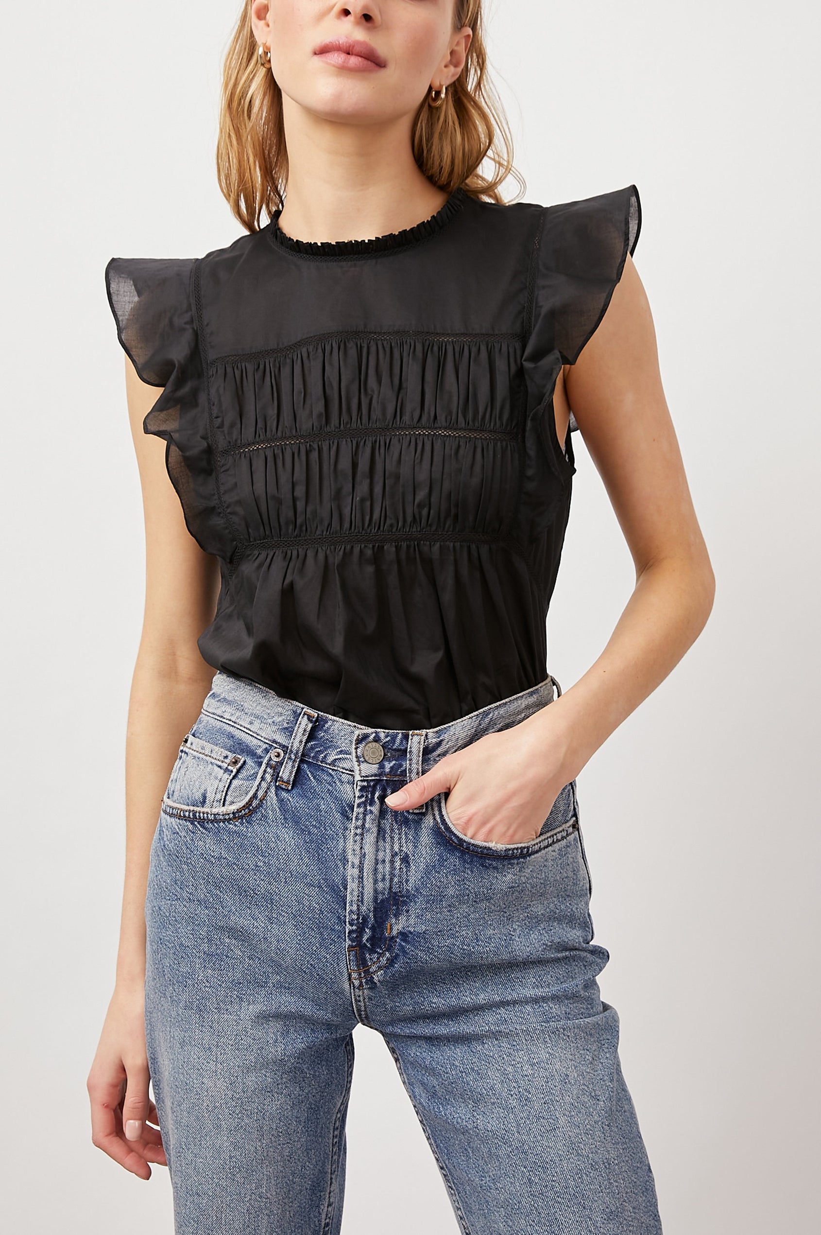 Filomena Short Sleeve Top with Flutter Sleeves, a Ruffled Neck, a Shirred Center Bodice, Lace Inserts and a Buttoned Keyhole at the Back in True Black Colorway - Front Tucked View Featured on Model