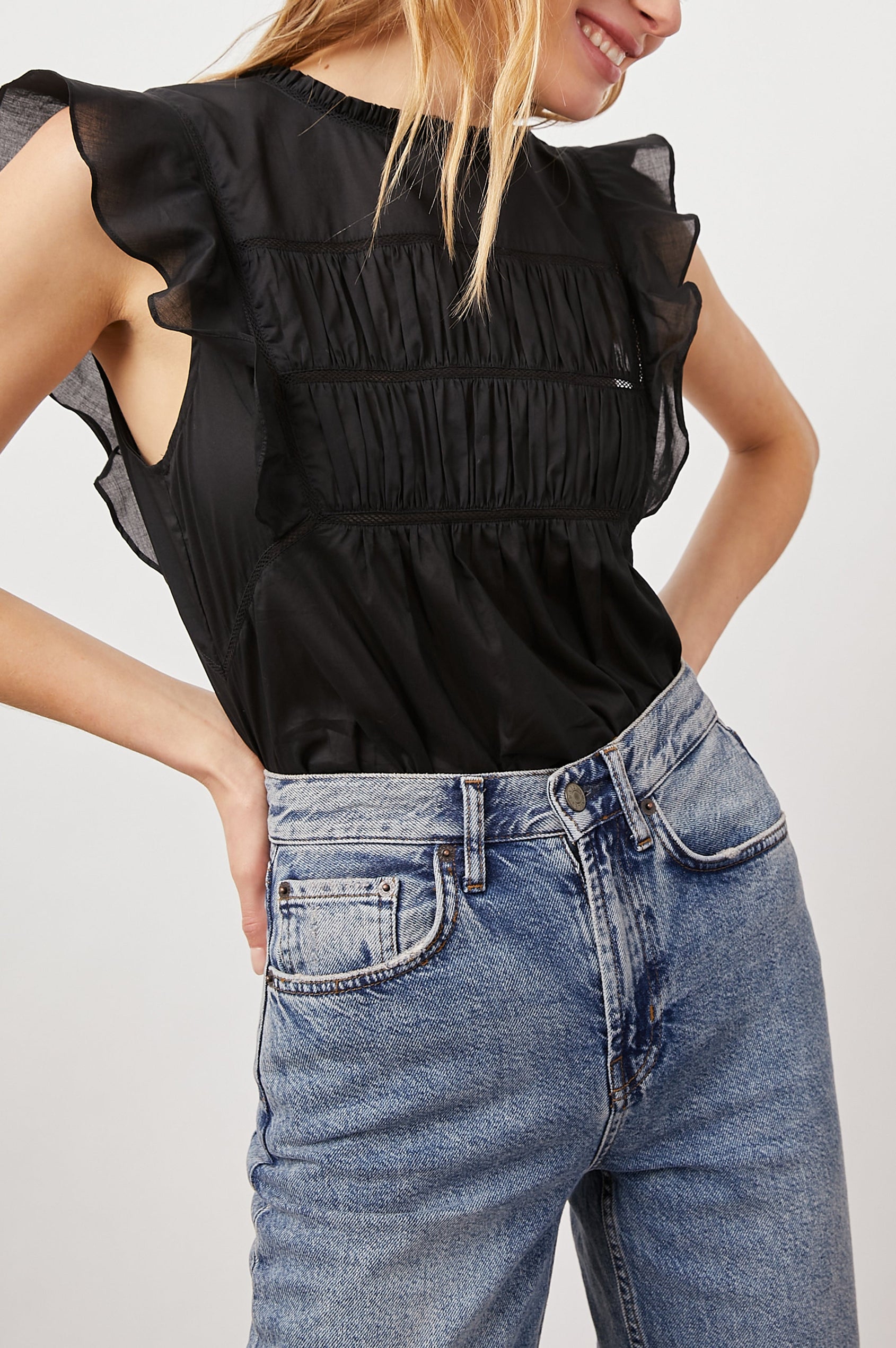 Filomena Short Sleeve Top with Flutter Sleeves, a Ruffled Neck, a Shirred Center Bodice, Lace Inserts and a Buttoned Keyhole at the Back in True Black Colorway - Front Tucked View Featured on Model