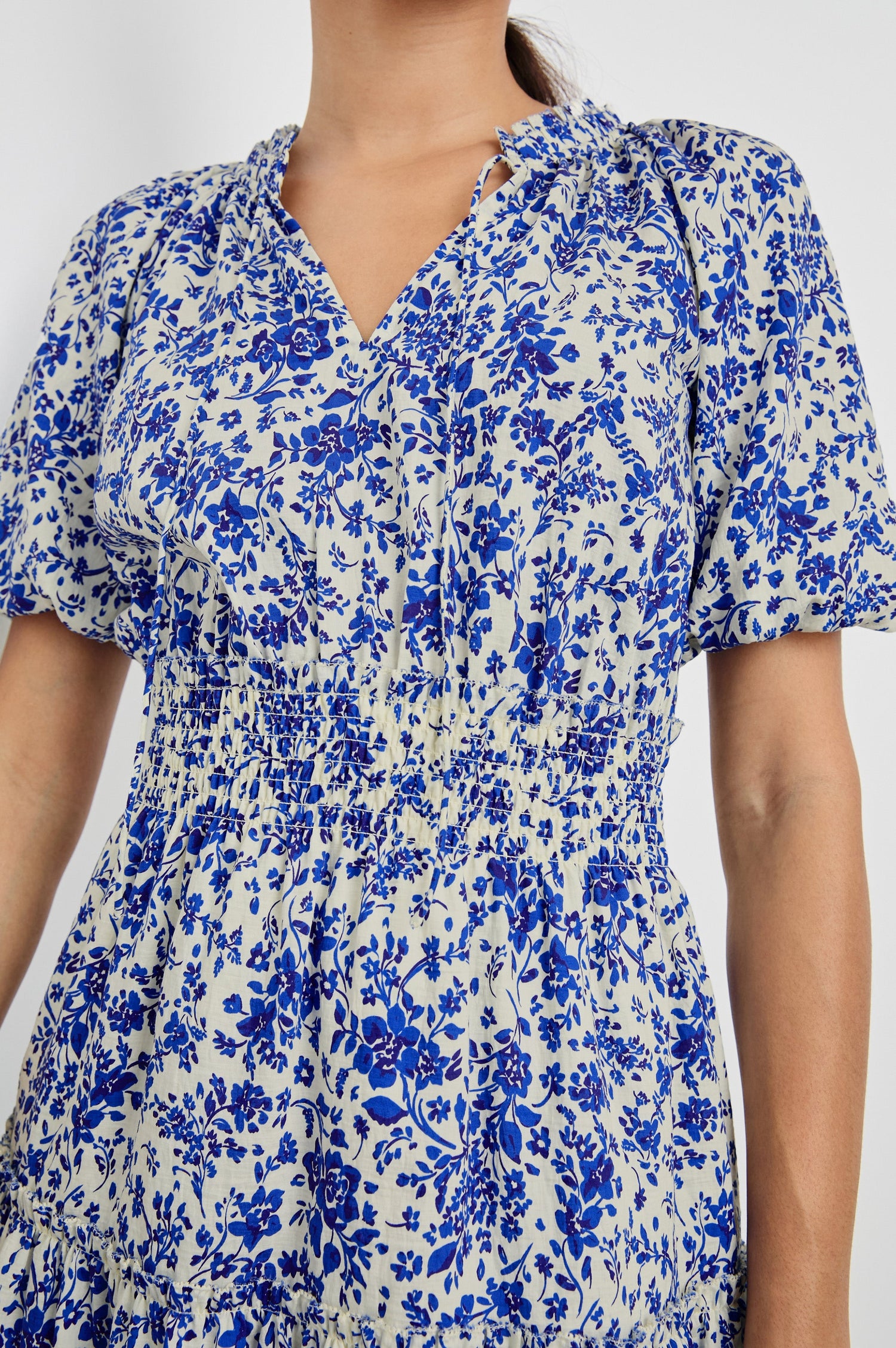 Fiorella Above-Knee Dress with Short Elasticated Puff Sleeves, Split V-Neck with Self Ties, and an Elasticated Ruched Waist Detail in Blue Marguerite Colorway. Front Detailed View Shown on Model.