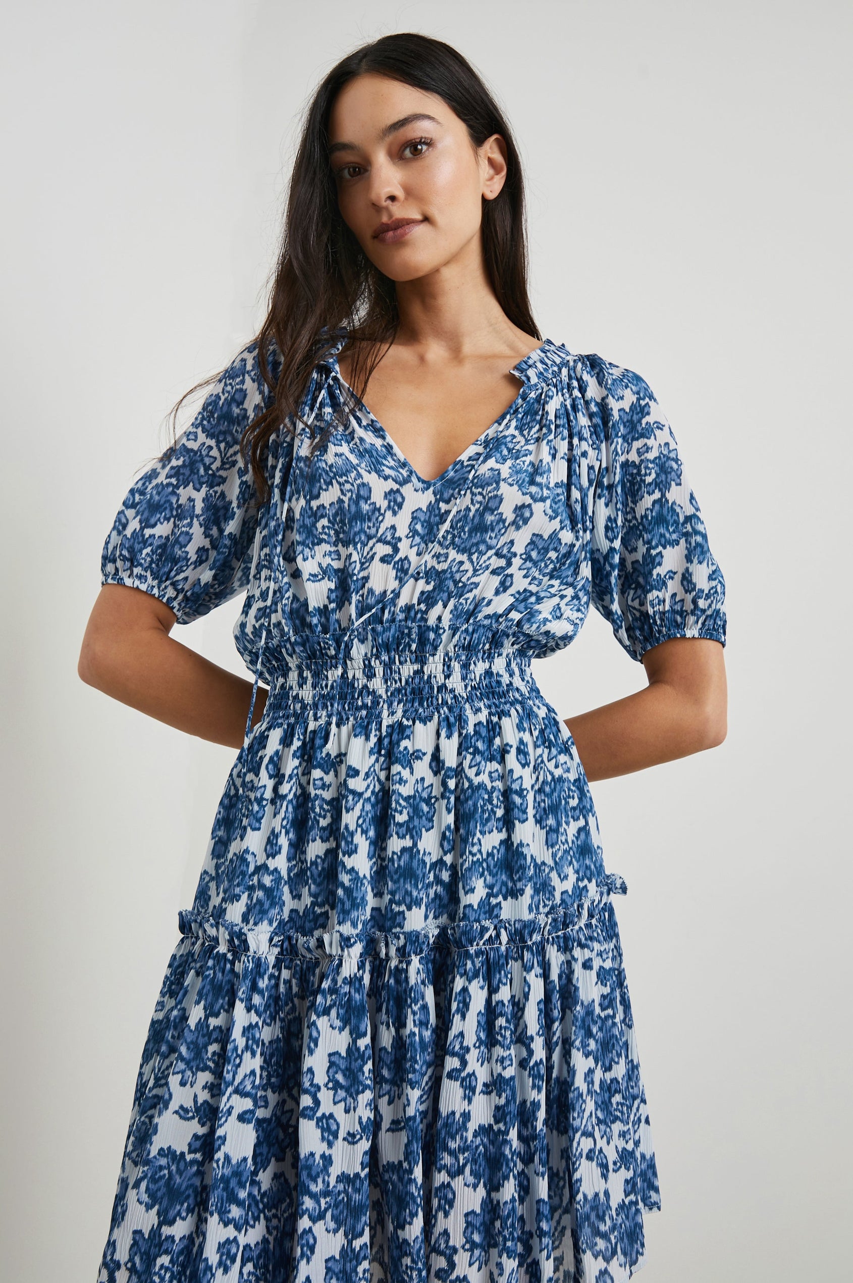 Fiorella Short-Sleeve, Above-Knee Dress with a Shirred Collar and Waist, V-neckline with Ties, Puff Sleeves and a Tiered Skirt in Chambray Floral Colorway, Blue Flowers on White - Front View Featured on Model
