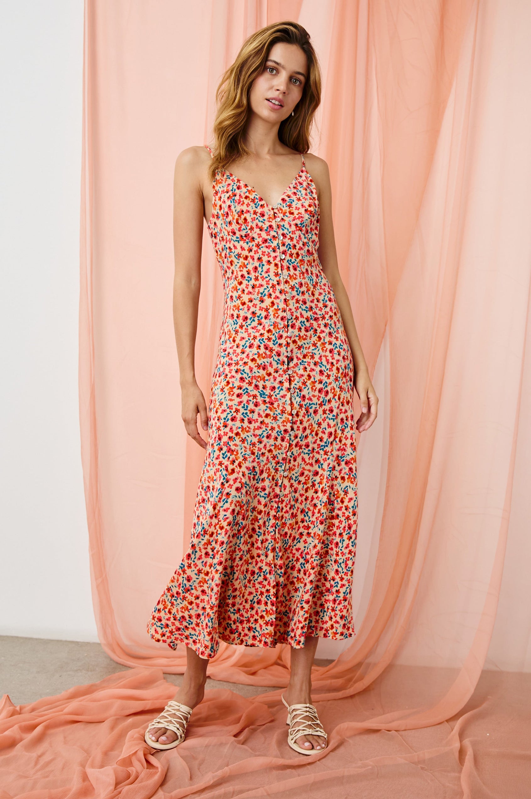 Florian Midi Dress with a V-Neckline, Spaghetti Straps, and Buttons down the front in Red Posy Colorway, Red, Blue and Orange on Tan - Front Full Body View Featured on model