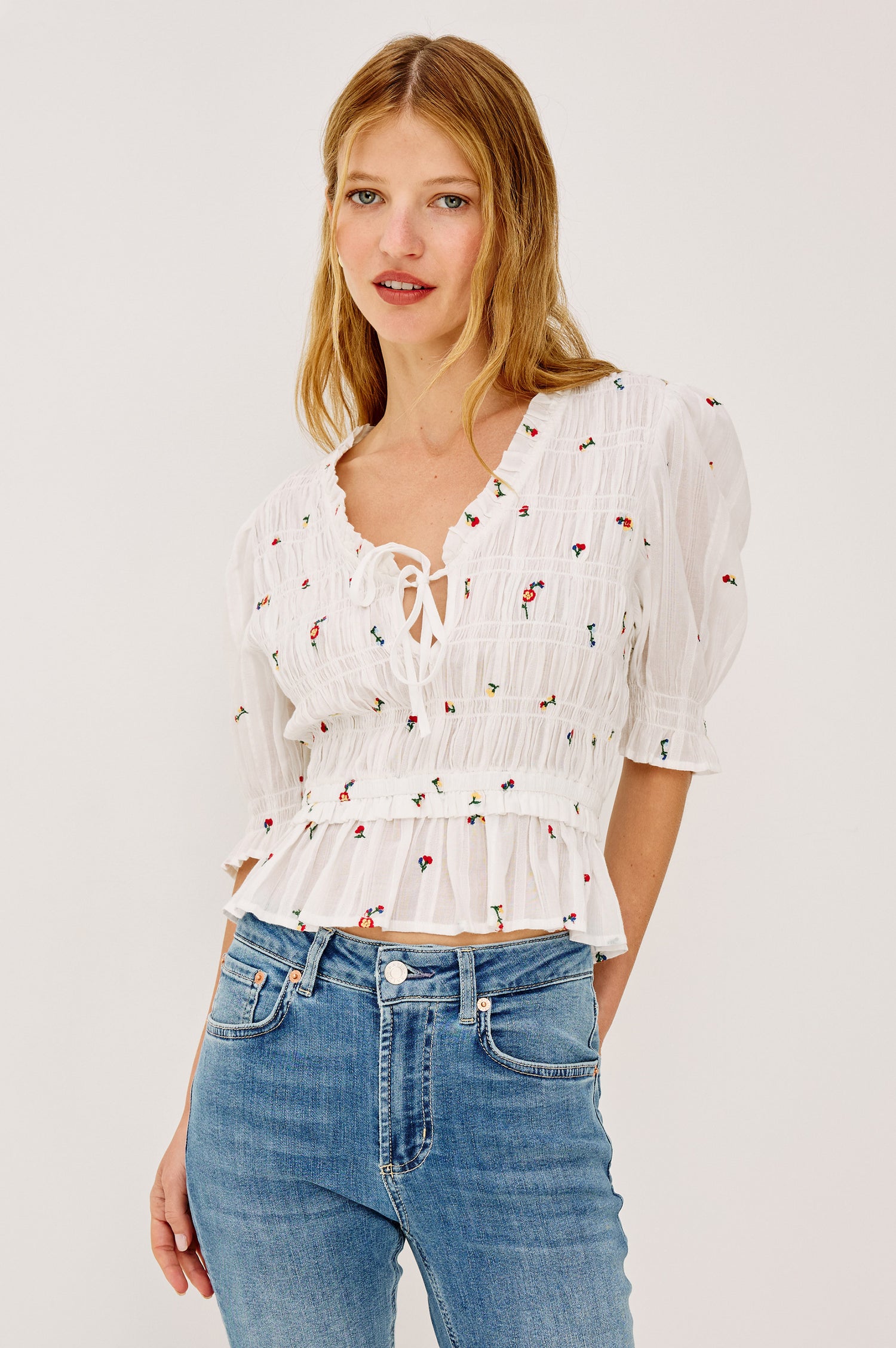 Fontaine Top in Cotton With Smocked Bodice, Self-Tie V-Neckline, Short Puff Sleeves, and Softly Flared Peplum Hem in White Wildflowers Colorway - Upper Body Front View Featured on Model