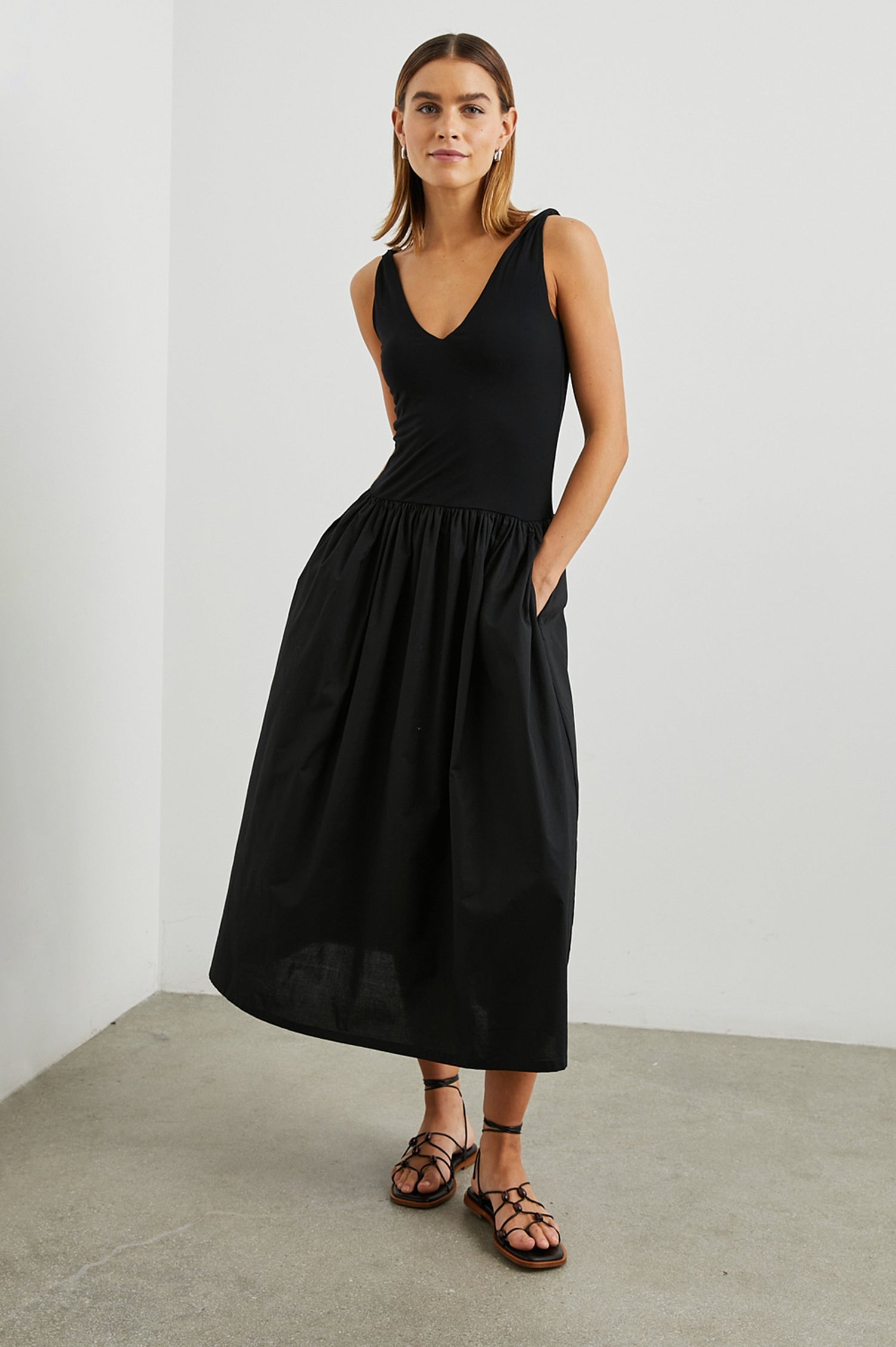Franca Sleeveless Midi Dress with Twisted Shoulder Straps, a deep V Neck and Pleats at the Waist in Black Colorway - Front Full Body View Featured on Model