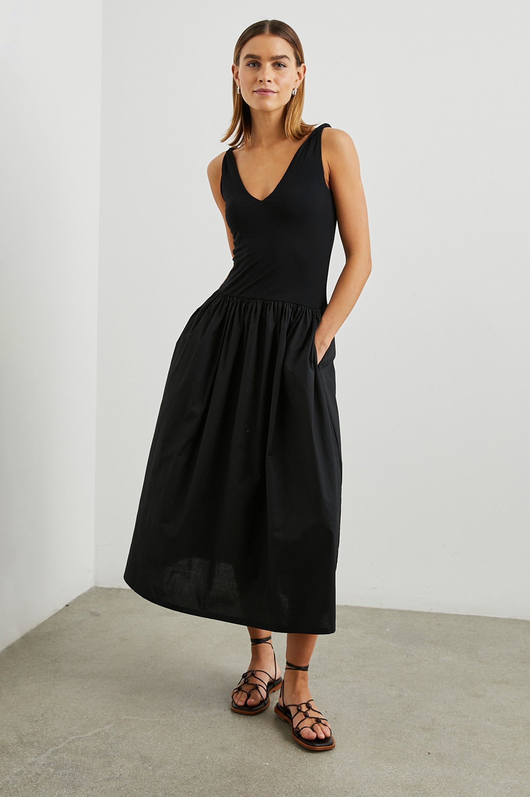 Franca Sleeveless Midi Dress with Twisted Shoulder Straps, a deep V Neck and Pleats at the Waist in Black Colorway - Front Full Body View Featured on Model