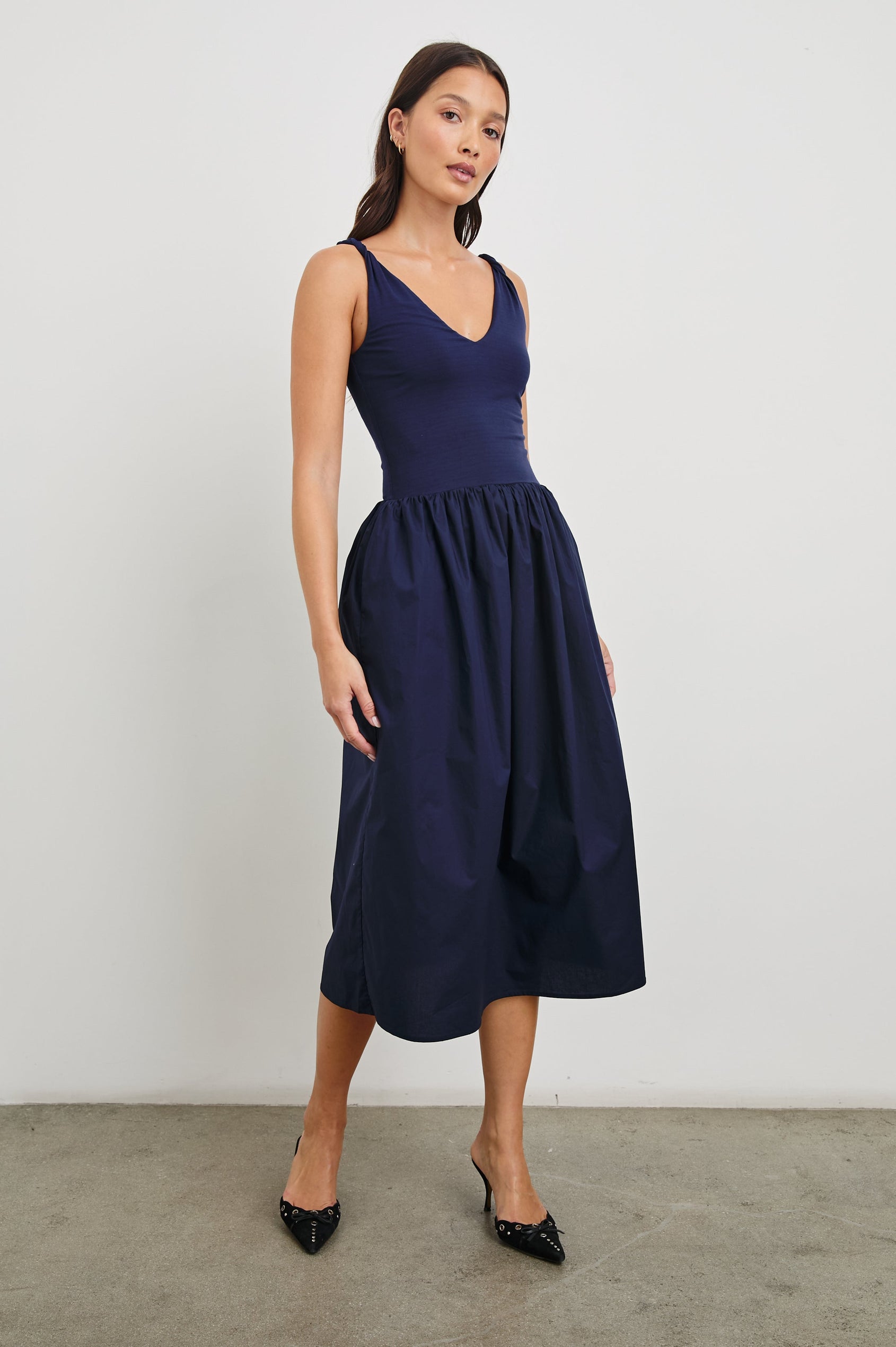 Franca Sleeveless Midi Dress with Twisted Shoulder Straps, a deep V Neck and Pleats at the Waist in Navy Colorway - Front Full Body View Featured on Model