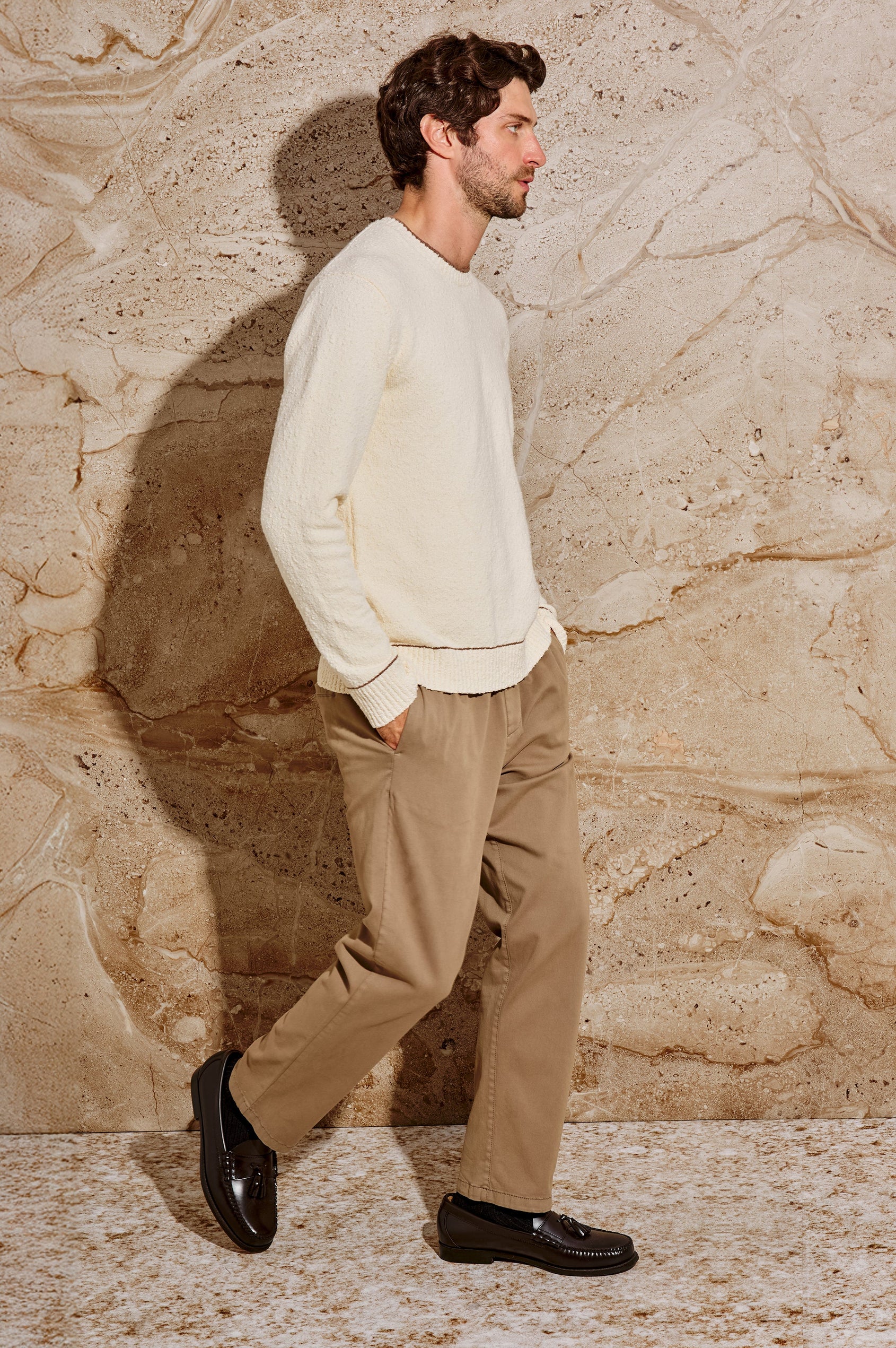 The Franco is a long sleeve crew neck sweater with contrast brown on neck, sleeve and hem in Cream colorway. Side full body view featured on model.