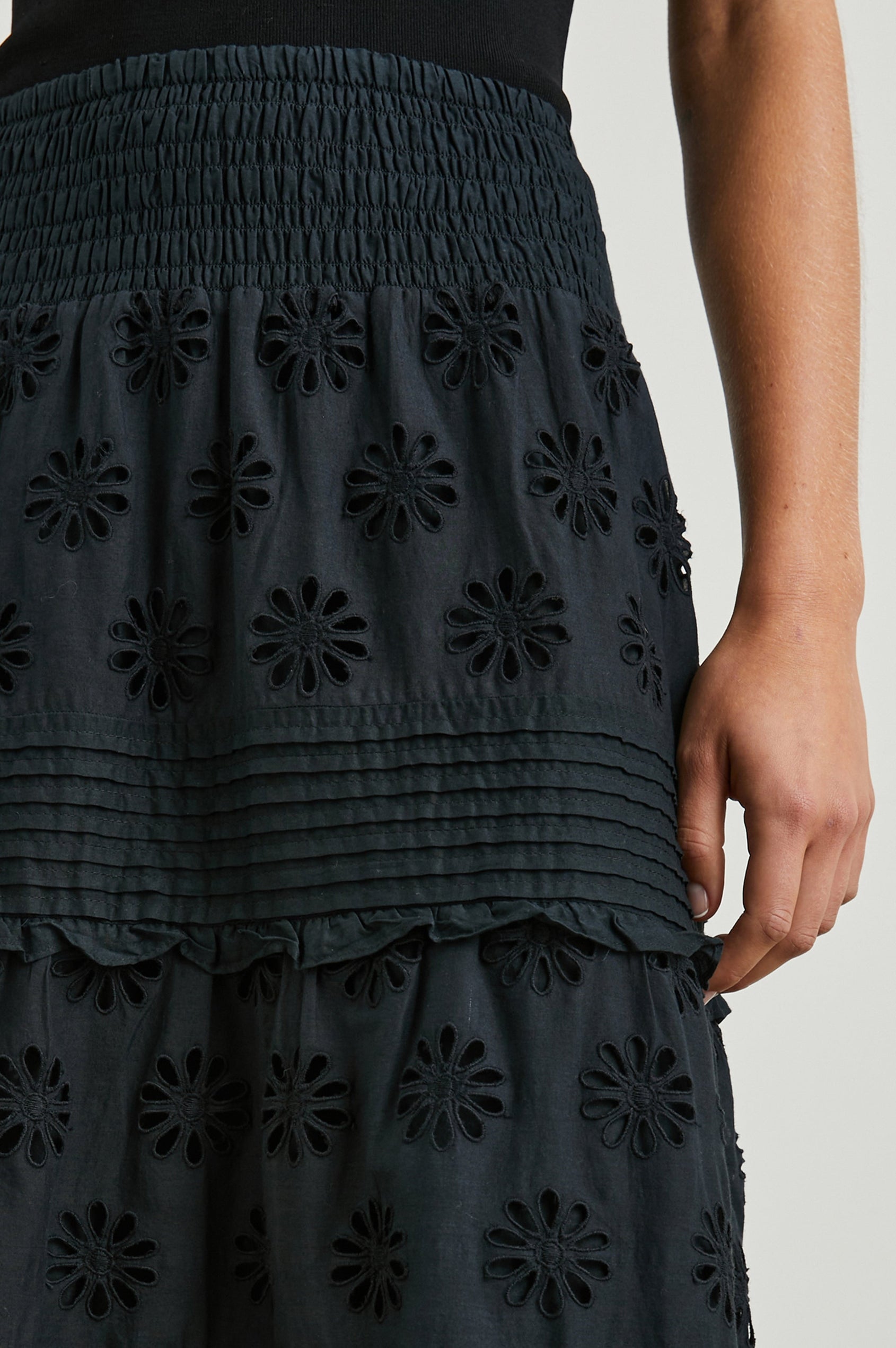 Gail Tiered Midi Skirt with a Shirred Waist, Horizontal Pleating and Ruffles, and Eyelet Flowers in Black Colorway - Front View Featured on Model 