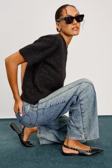 Getty Twist Seam Wide Leg Denim Pants with a Diagonal Seam Across the Leg, Belt Loops, Two Front Pockets and Two Back Patch Pockets in Desert Sky Colorway - Side Kneeling View Featured on Model