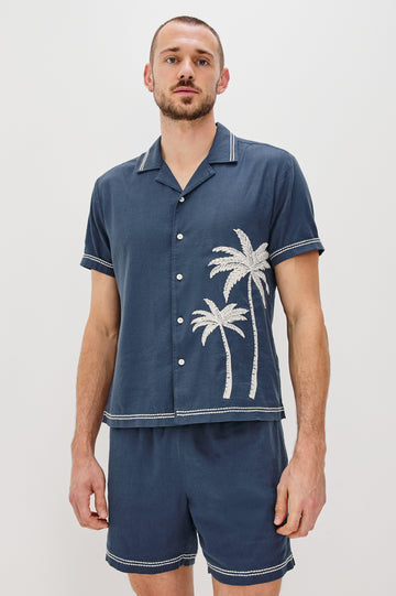 Gibson Button Front Shirt with Open Relaxed Collar, Short Sleeves, White Contrast Buttons, Contrast White Stitching at Collar and Hems and Embroidered White Palm Trees on Left Side in Navy White Palm Colorway. Front View Shown on Model.