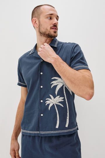 Gibson Button Front Shirt with Open Relaxed Collar, Short Sleeves, White Contrast Buttons, Contrast White Stitching at Collar and Hems and Embroidered White Palm Trees on Left Side in Navy White Palm Colorway. Front View Shown on Model.