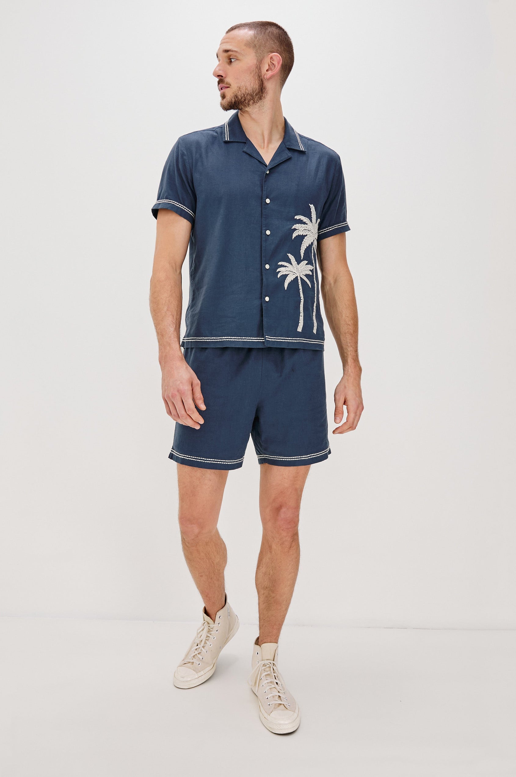 Gibson Button Front Shirt with Open Relaxed Collar, Short Sleeves, White Contrast Buttons, Contrast White Stitching at Collar and Hems and Embroidered White Palm Trees on Left Side in Navy White Palm Colorway. Full Body Front View Shown on Model.