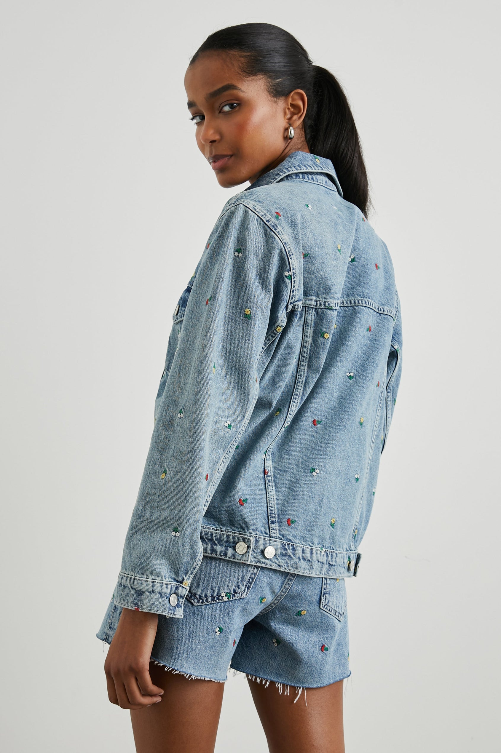 Grove Boyfriend Trucker Denim Jacket with Button Closure, Two Front Pockets, Two Chest Button Flap Pockets, Front Vertical Seams in Flower Field Colorway, with Embroidered Daisies in Yellow, Red and White - Back View Featured on Model  