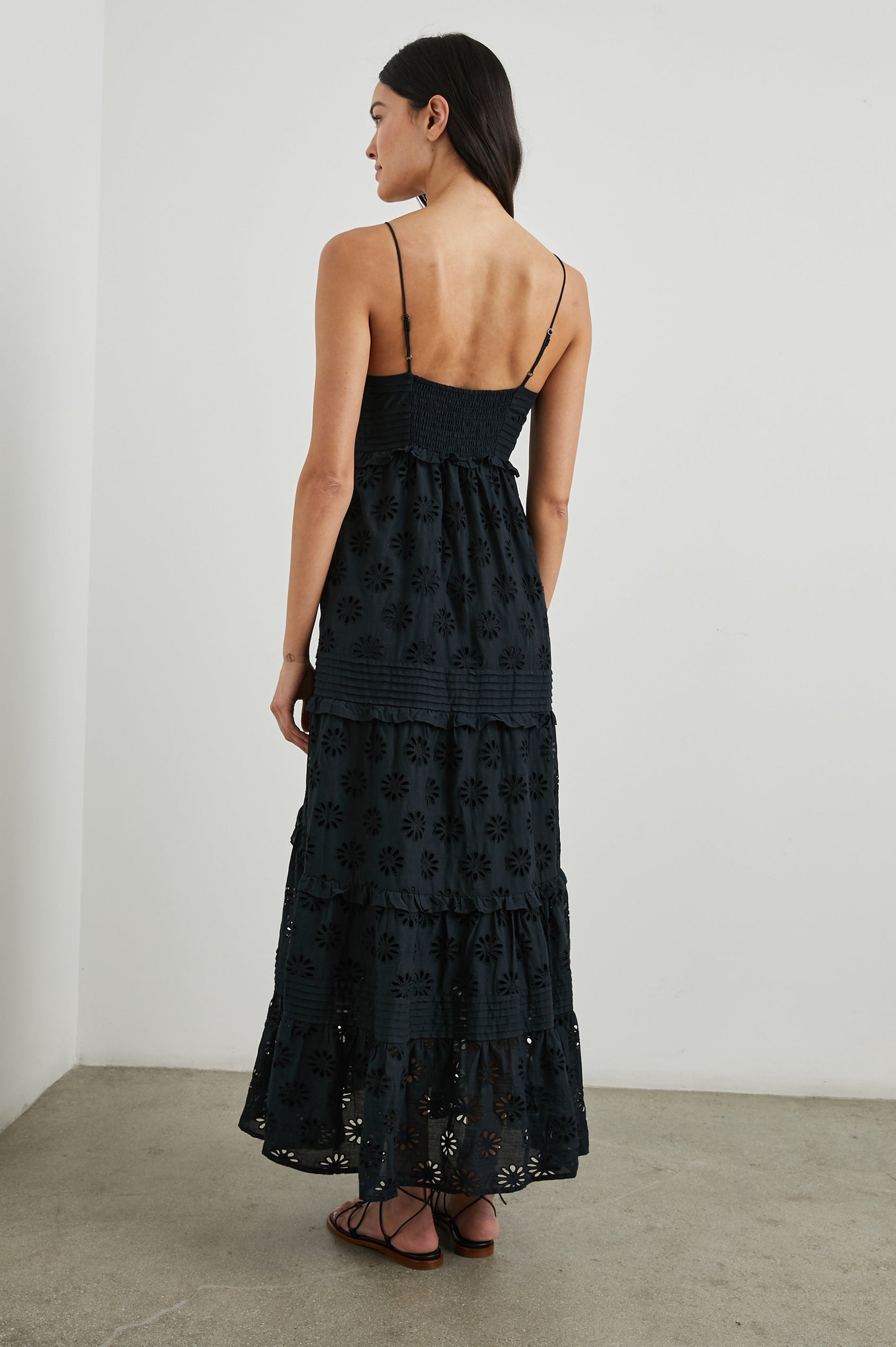 Henrietta Sleeveless Maxi Dress with Adjustable Spaghetti Straps, a Deep V Neck, Buttons Down the Front, a Shirred Back Bodice, a Tiered Skirt with Ruffles and Horizontal Pleats, and a Floral Eyelet Design in Black Colorway - Back Full Body View Featured on Model 