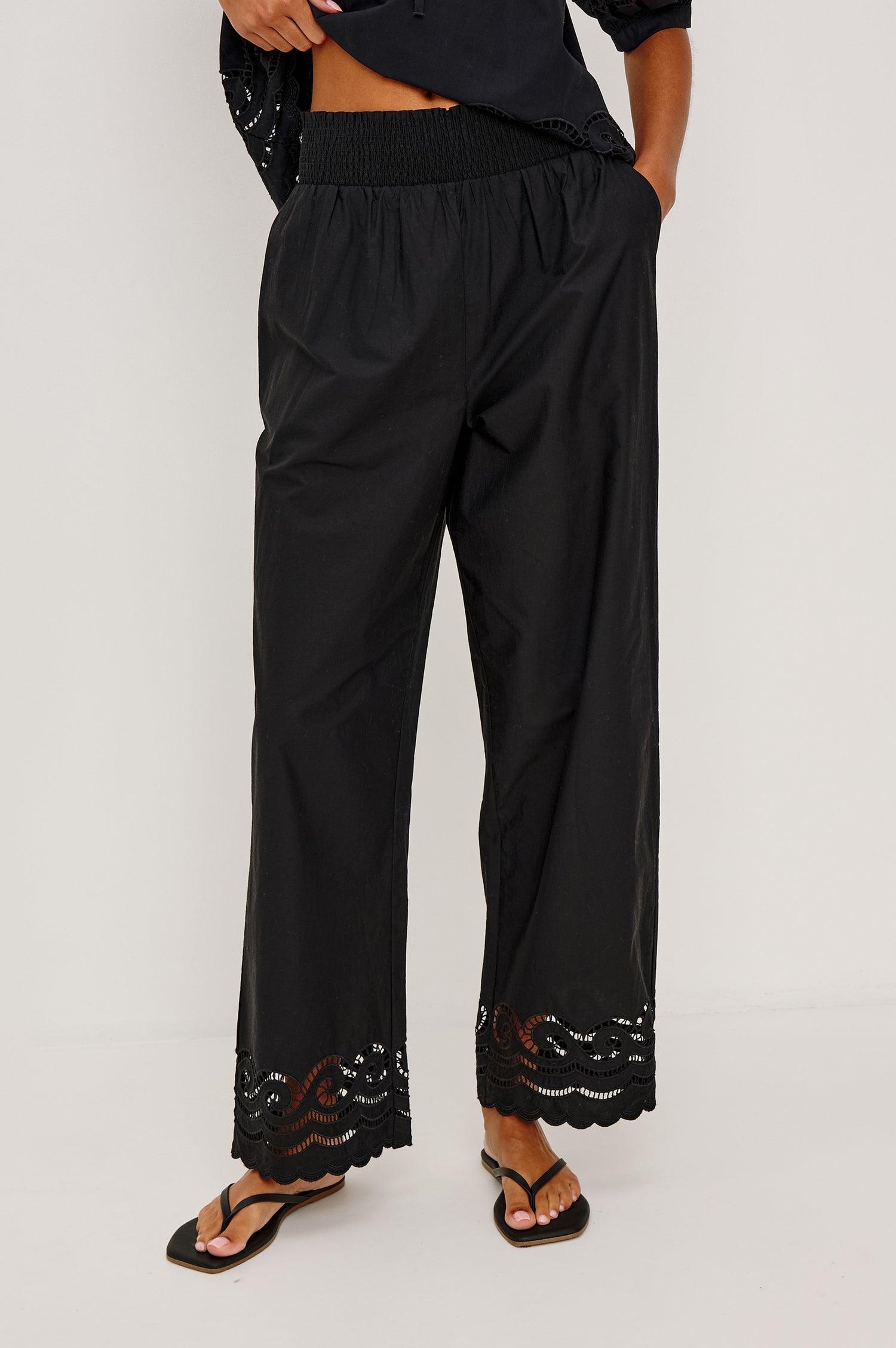 Henrik High-Rise High-Waisted Pant With Wide Smocked Waistband, Side Pockets, Straight Legs, and Scalloped Ladder Embroidered Hem in Black Colorway - Lower Body Front View Featured on Model