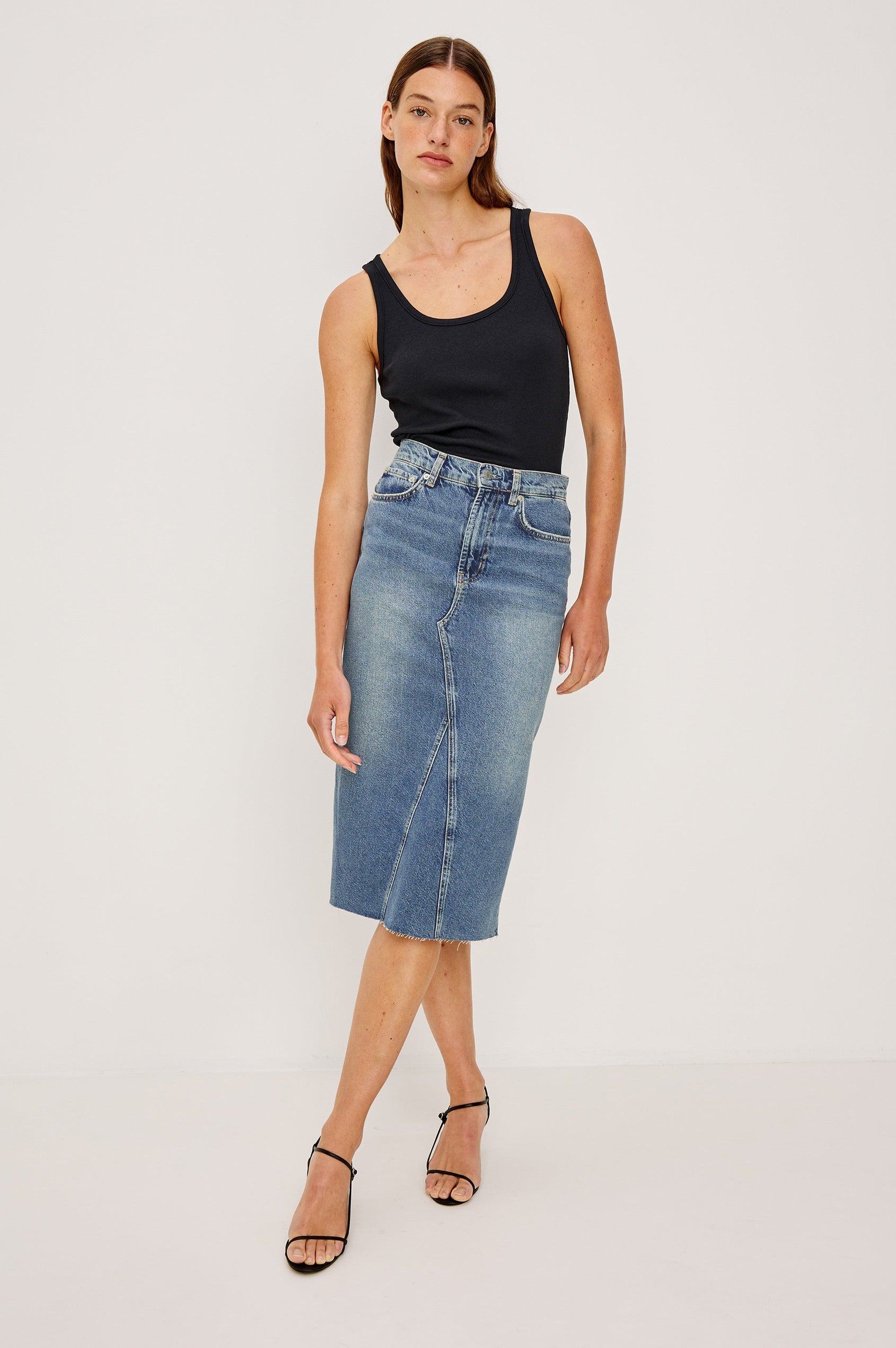 Highland Denim Midi Skirt with a Raw Hem, a Back Vent, Additional Front Seams, Belt Loops, Two Front Pockets plus a Coin Pocket and Two Back Patch Pockets in Vintage Sapphire Colorway - Front Full Body View Featured on Model 