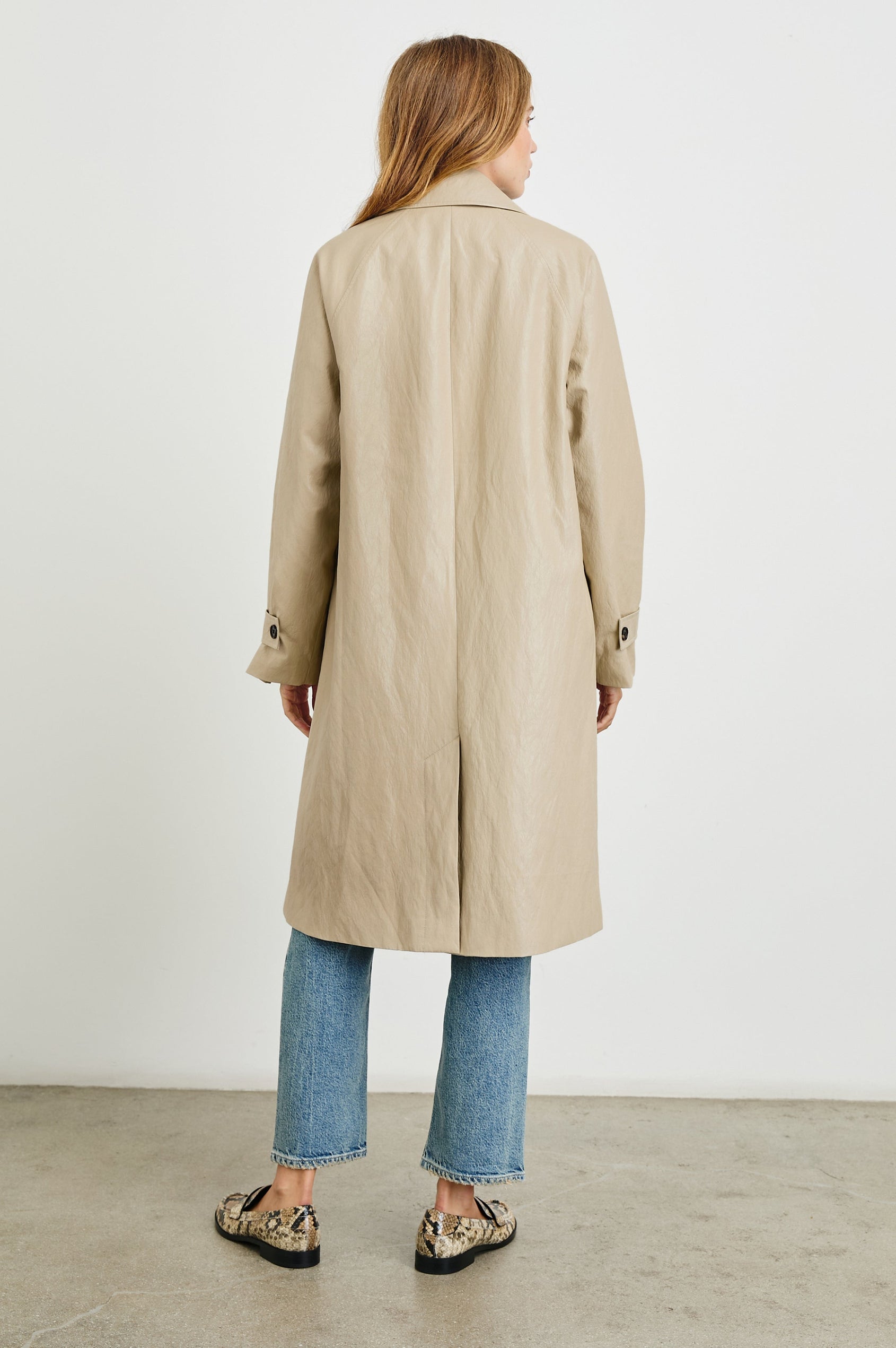 Hills Knee-Length Faux Leather Jacket with Button Closure, a Hidden Placket, Two Front Pockets, and Button Tabs at the Cuffs in Dune Colorway - Back Full Body View Featured on Model 