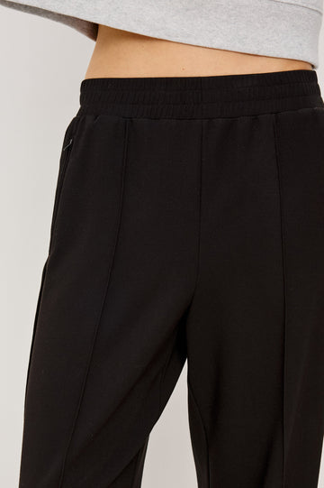Black ponte pull-on pants with an elastic waistband. The pants feature functional ankle zippers that can be opened to create a subtle flare. Close Up View on Model.