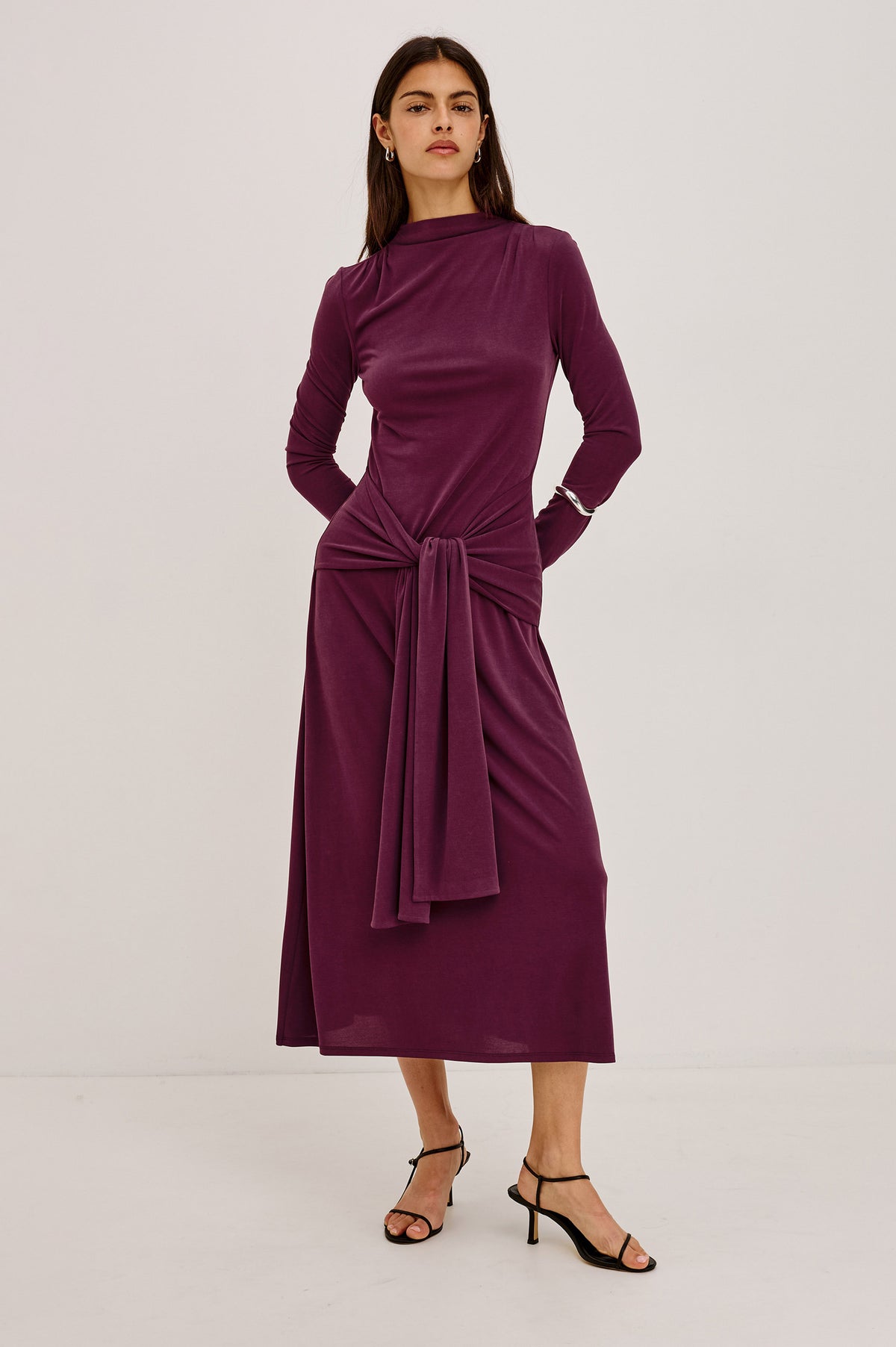 Hollis Midi Dress in Soft Jersey With Mockneck, Front Waist Ties, Pleated Shoulders, Long Sleeves, and A-Line Skirt in Wine Colorway - Front View Featured on Model.