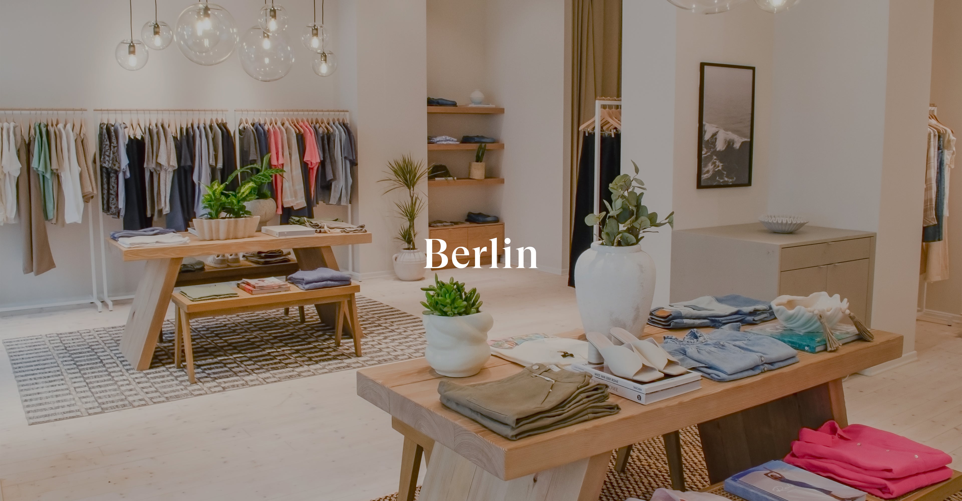 INSIDE OF BERLIN STORE SHOWING MULTIPLE TABLES IN THE MIDDLE OF THE ROOM WITH CLOTHING FOLDED ON TOP OF THEM