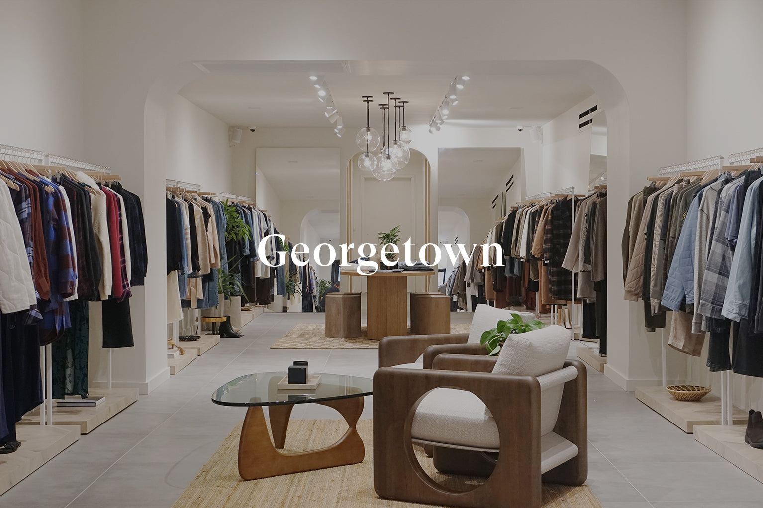 INSIDE OF GEORGETOWN STORE SHOWING ONE ROOM WITH MULTIPLE CLOTHING RACKS OF CLOTHING AGAINST EACH WALL AND TWO CHAIRS IN THE CENTER OF THE ROOM