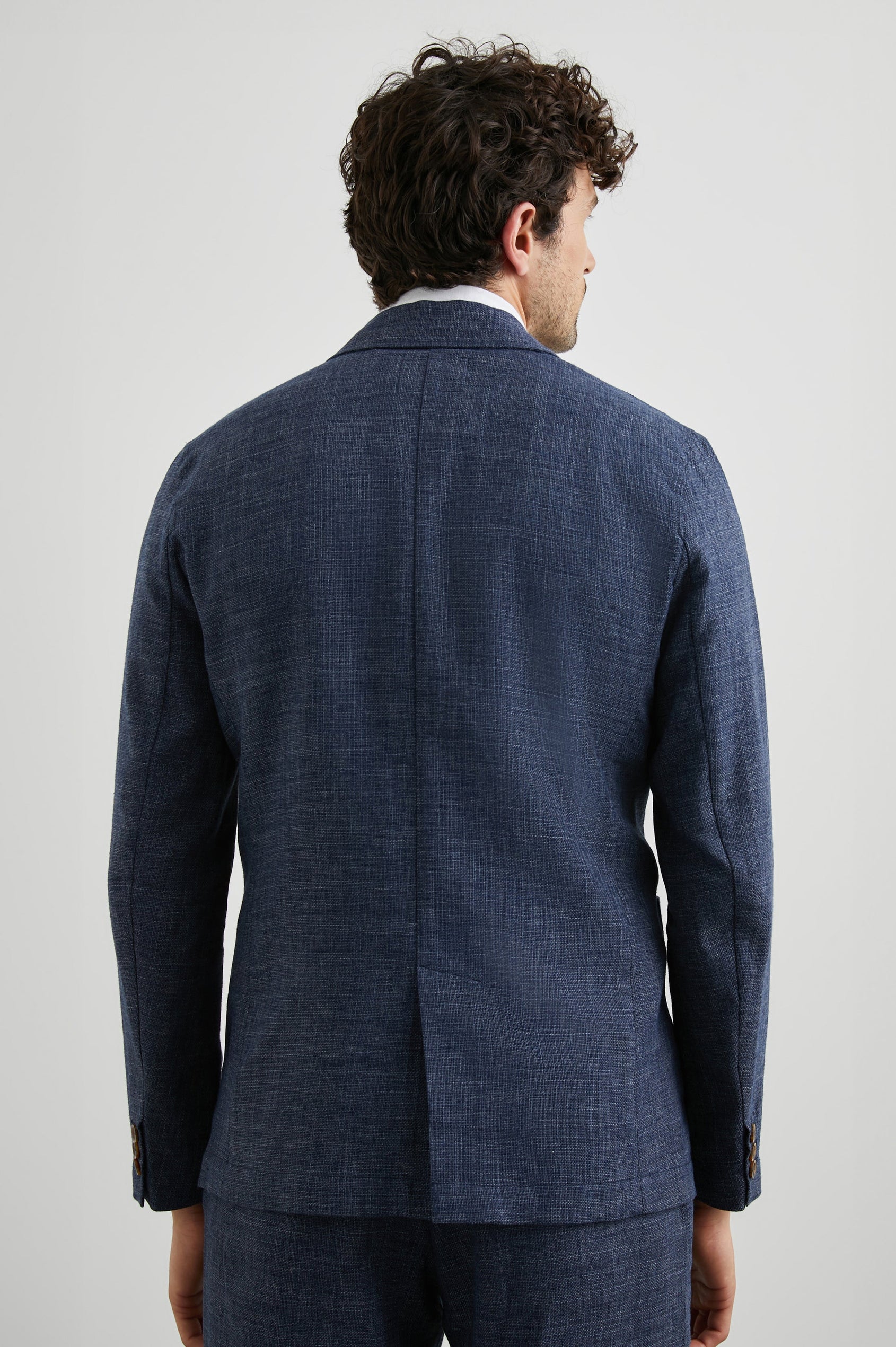 Idris Blazer with Two Button Closure, Two Front Patch Pockets, a Chest Patch Pocket and Three-Button Cuffs in Navy Melange Colorway - Back View Featured on Model