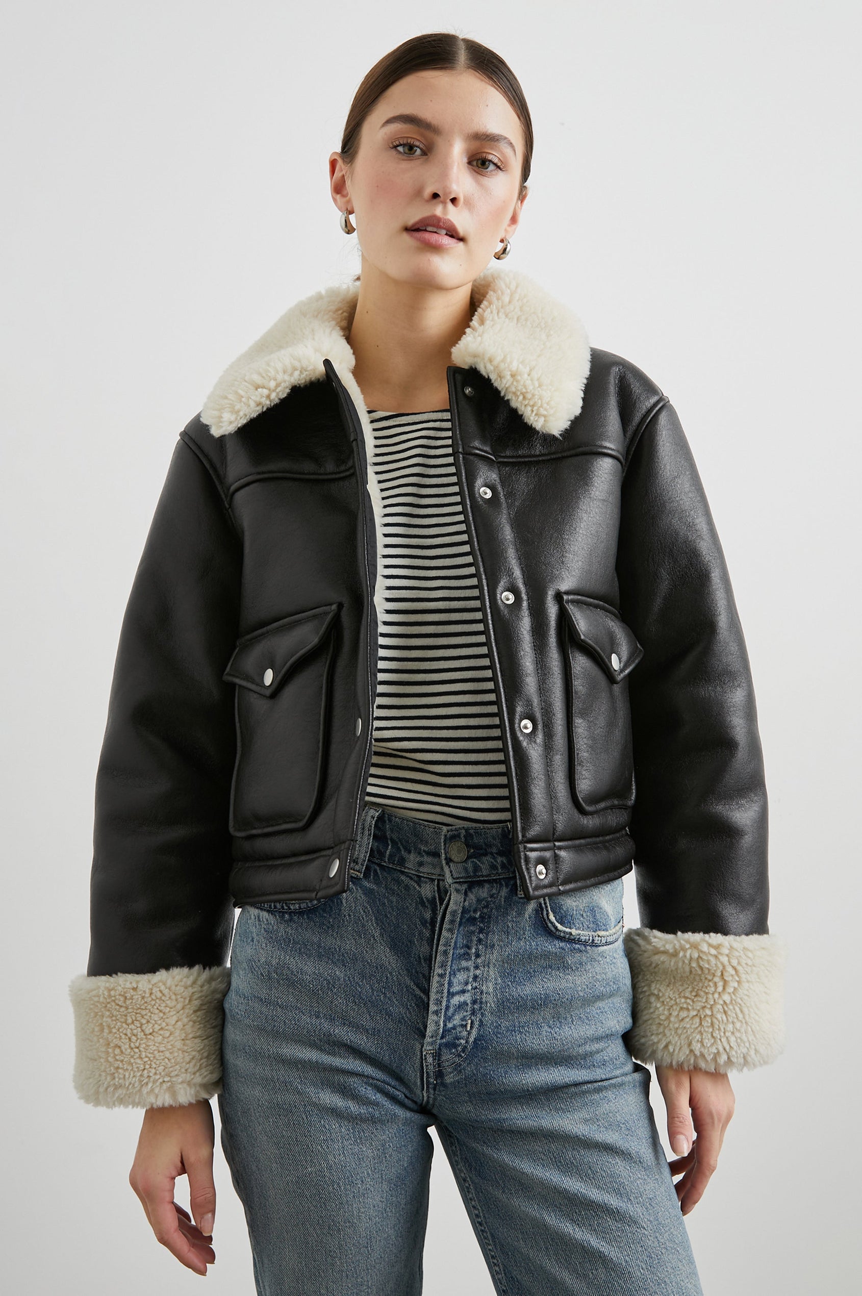 Imani Cropped Faux Leather Jacket with Silver-Toned Snap Closure, Two Front Snap Flap Pockets and Ivory Faux Shearling Lining, Collar and Cuffs in Black Ivory Colorway - Front View Featured on Model  