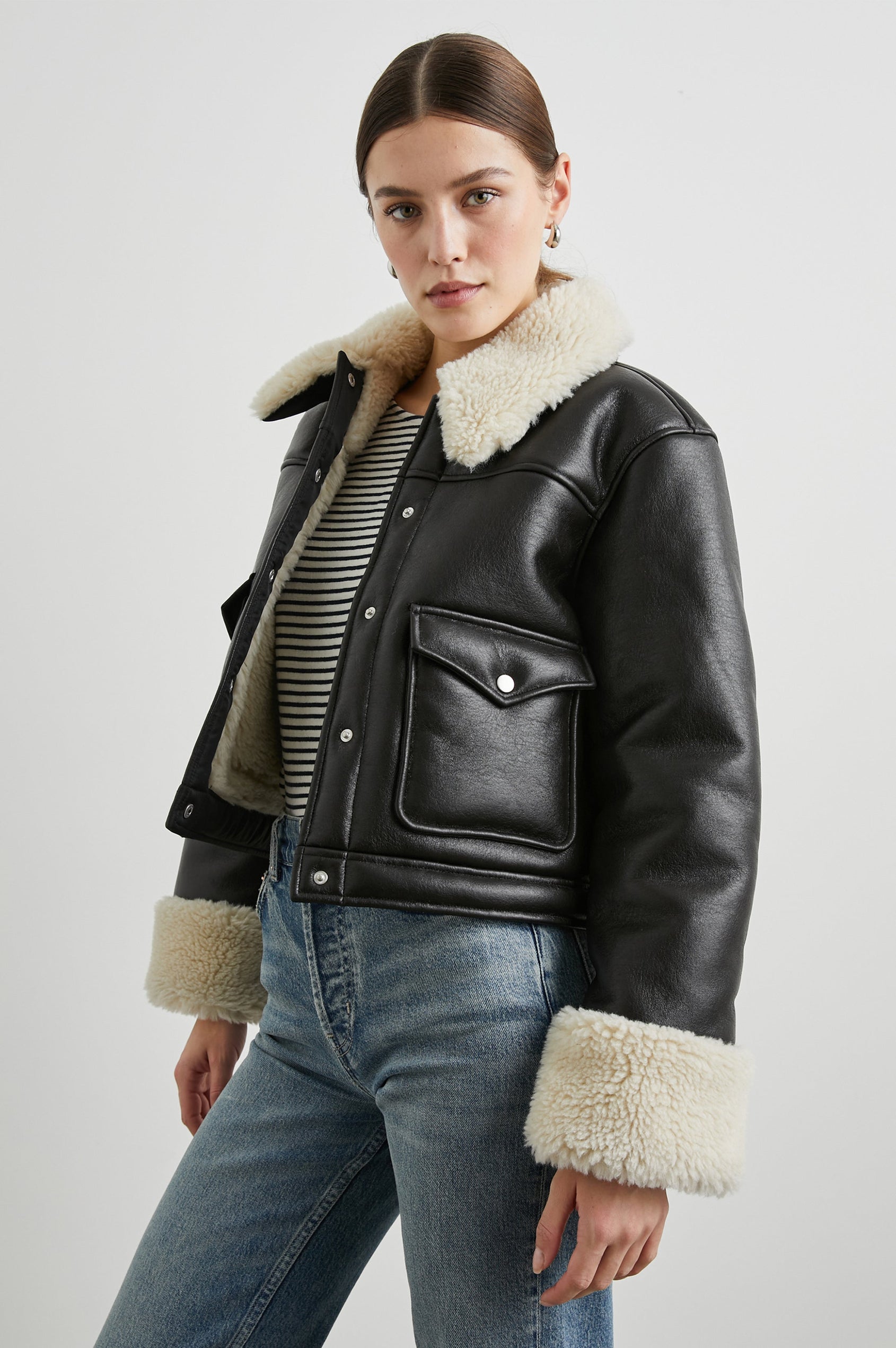 Imani Cropped Faux Leather Jacket with Silver-Toned Snap Closure, Two Front Snap Flap Pockets and Ivory Faux Shearling Lining, Collar and Cuffs in Black Ivory Colorway - Front View Featured on Model  