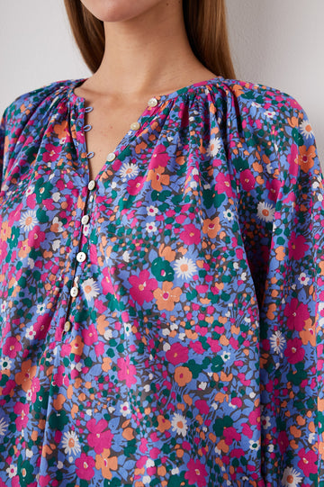 Indi Top with a V Neckline with a Button Placket, Pleating at Back Neckline and Elastic Cuffs in Leilani Floral Colorway, with pink, orange, green and white flowers - Front View Featured on Model