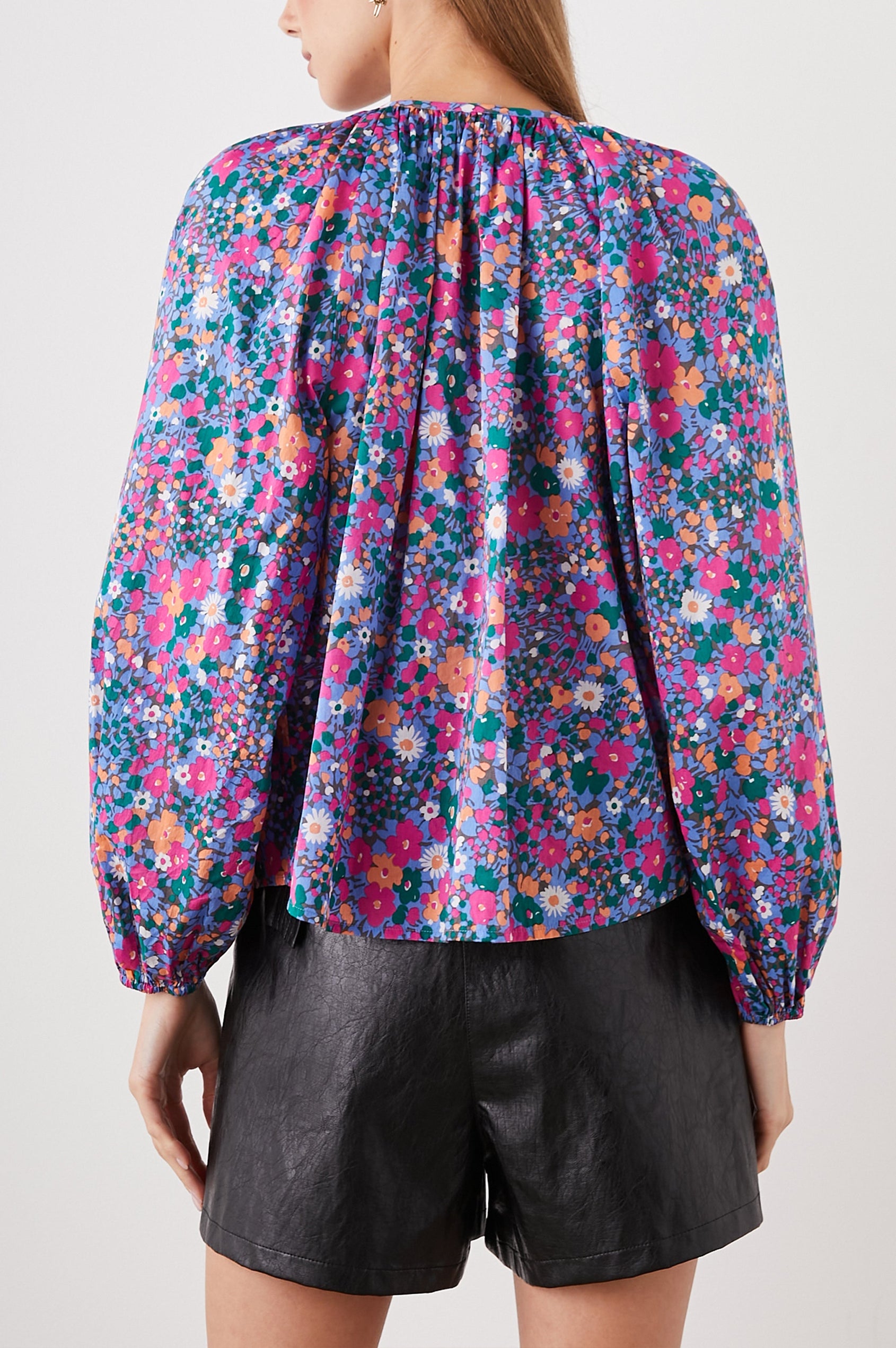 Indi Top with a V Neckline with a Button Placket, Pleating at Back Neckline and Elastic Cuffs in Leilani Floral Colorway, with pink, orange, green and white flowers - Back View Featured on Model