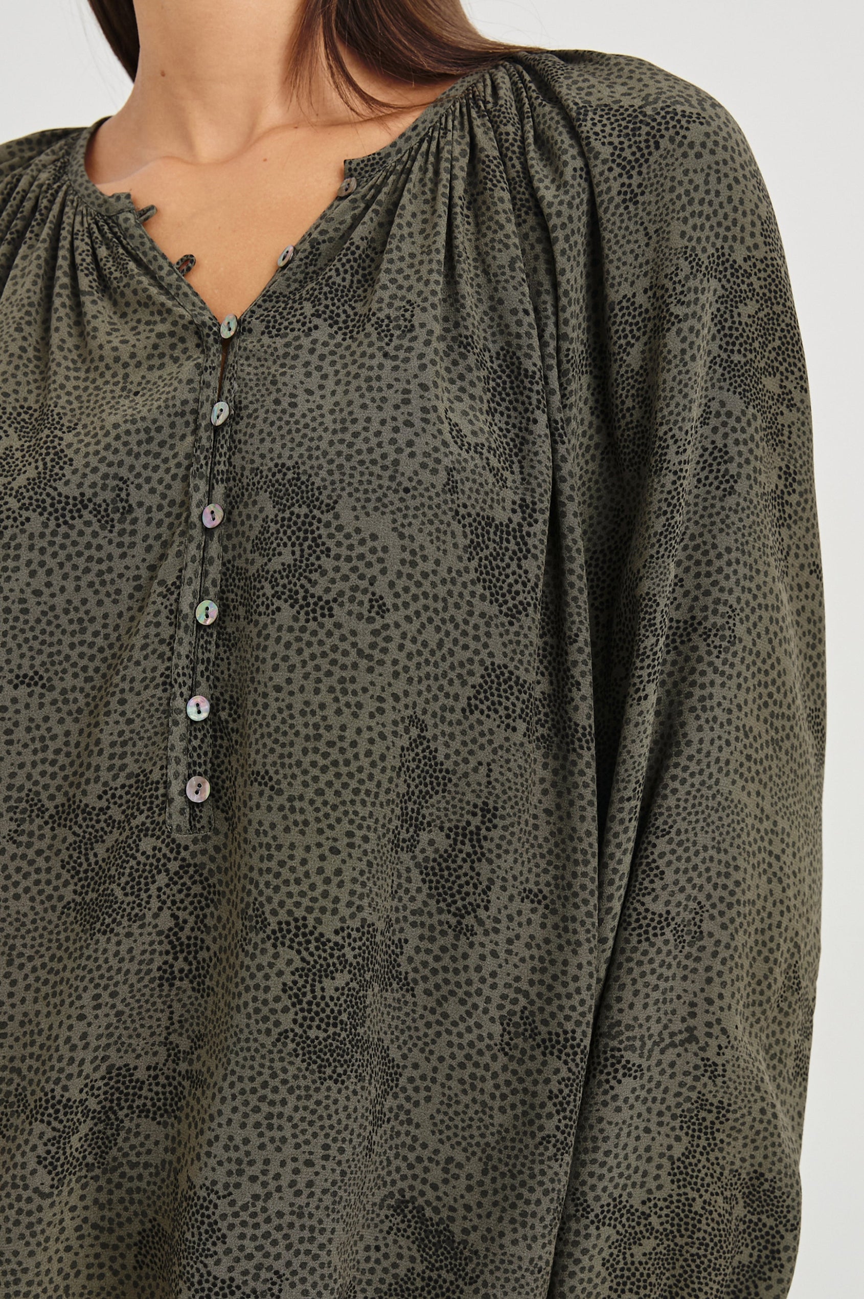 Indi Top with a V Neckline with a Button Placket, Pleating at Back Neckline and Elastic Cuffs in Olive Pebble Colorway, with black pebbles on olive - Front Untucked View Featured on Model