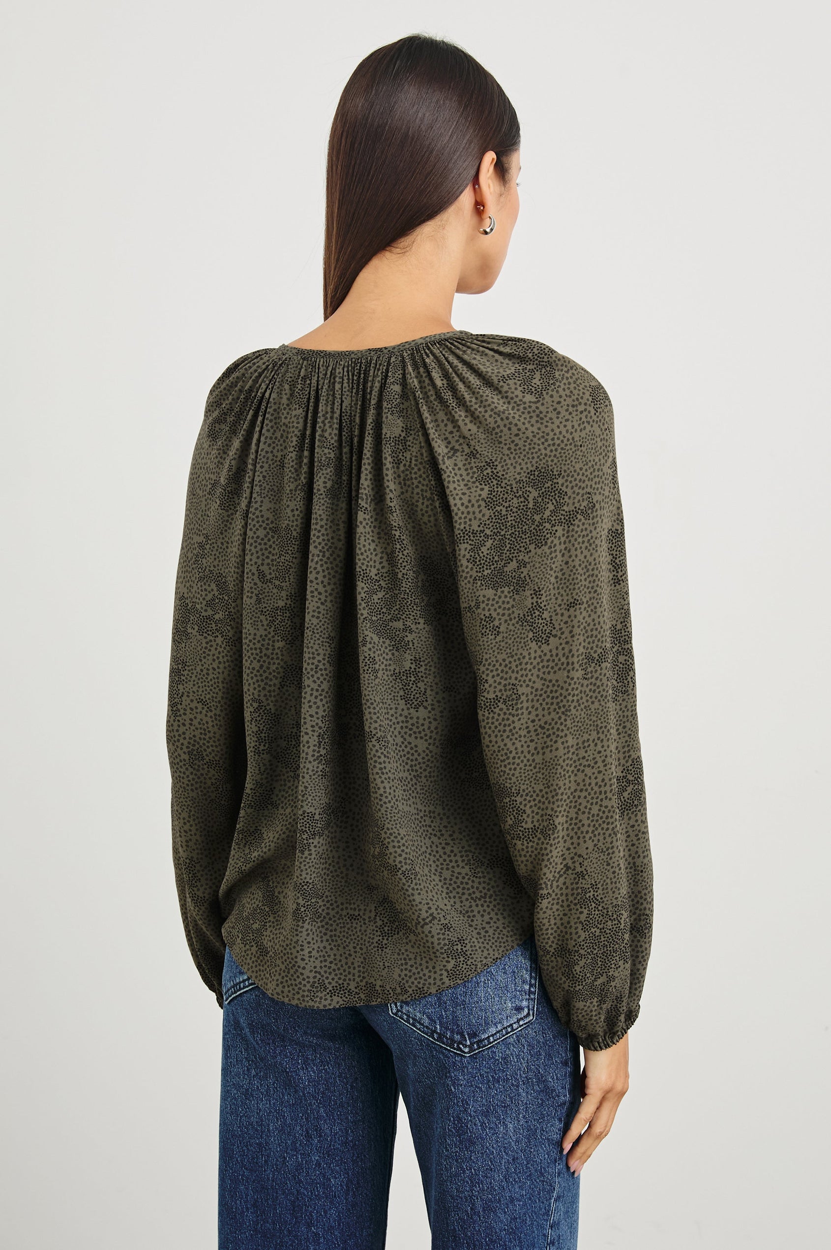 Indi Top with a V Neckline with a Button Placket, Pleating at Back Neckline and Elastic Cuffs in Olive Pebble Colorway, with black pebbles on olive - Back Untucked View Featured on Model