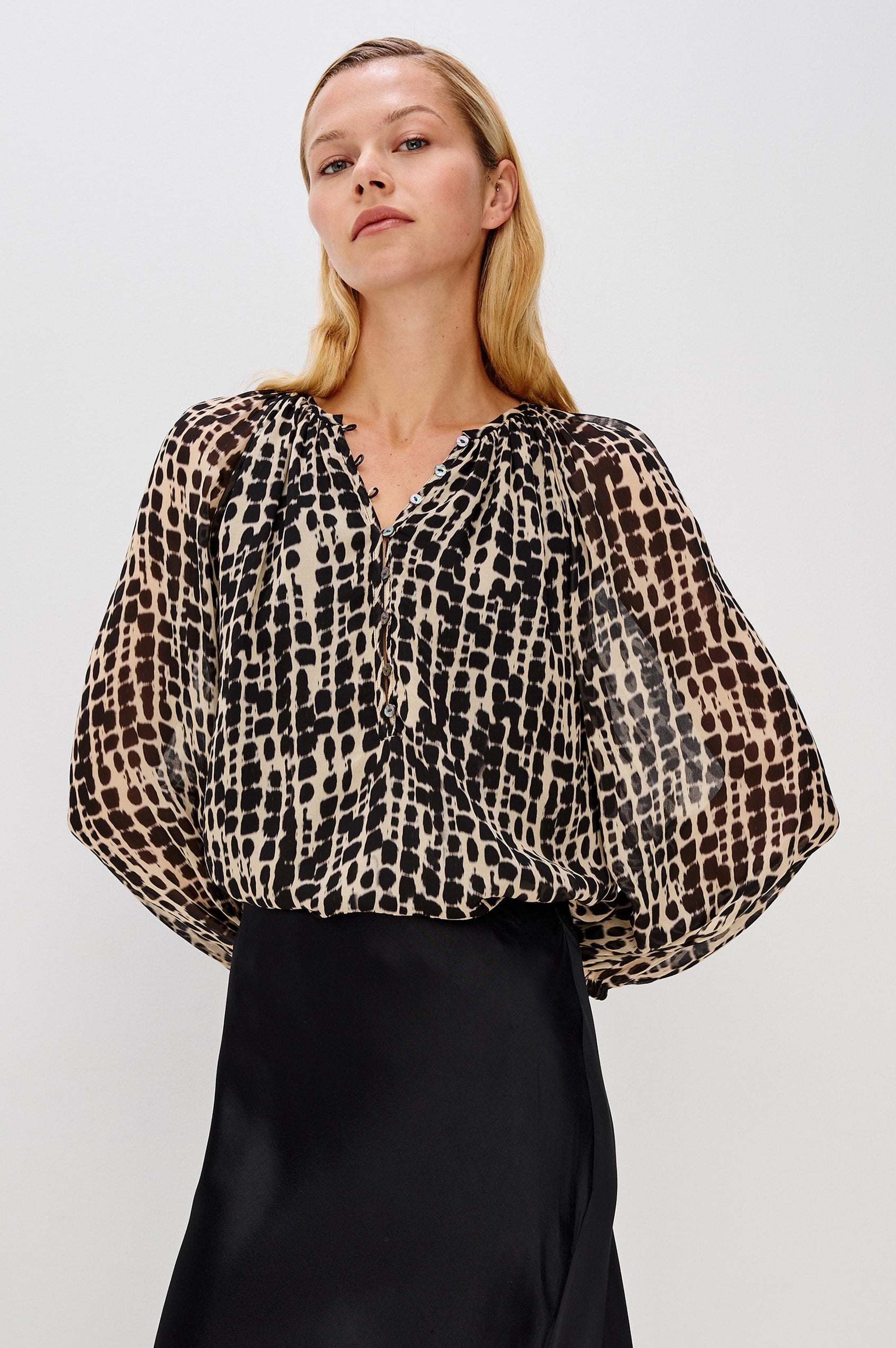 Flowy, 1960s-inspired blouse with a spotted shibori print. The top has sheer, voluminous sleeves with elastic cuffs, natural shell buttons, and a babydoll silhouette. Front View on Model.