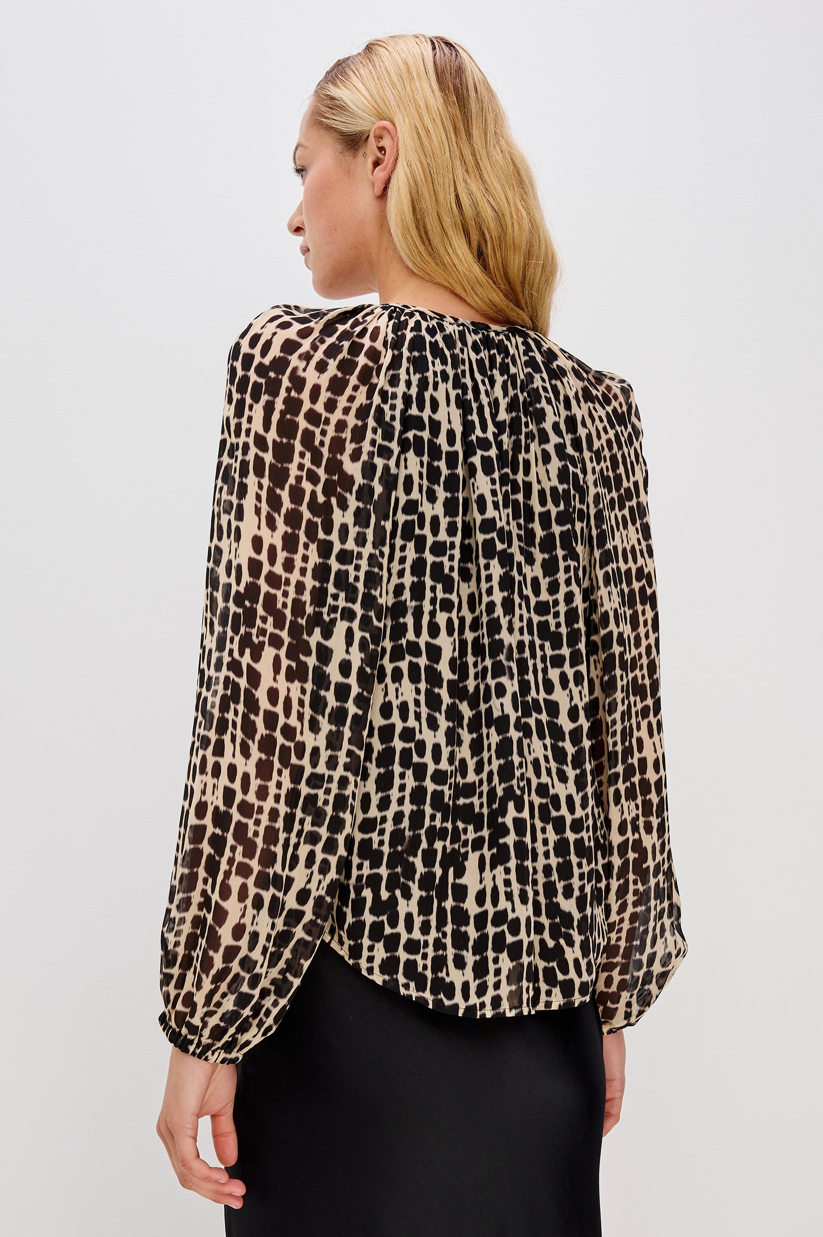 Flowy, 1960s-inspired blouse with a spotted shibori print. The top has sheer, voluminous sleeves with elastic cuffs, natural shell buttons, and a babydoll silhouette. Back View on Model.