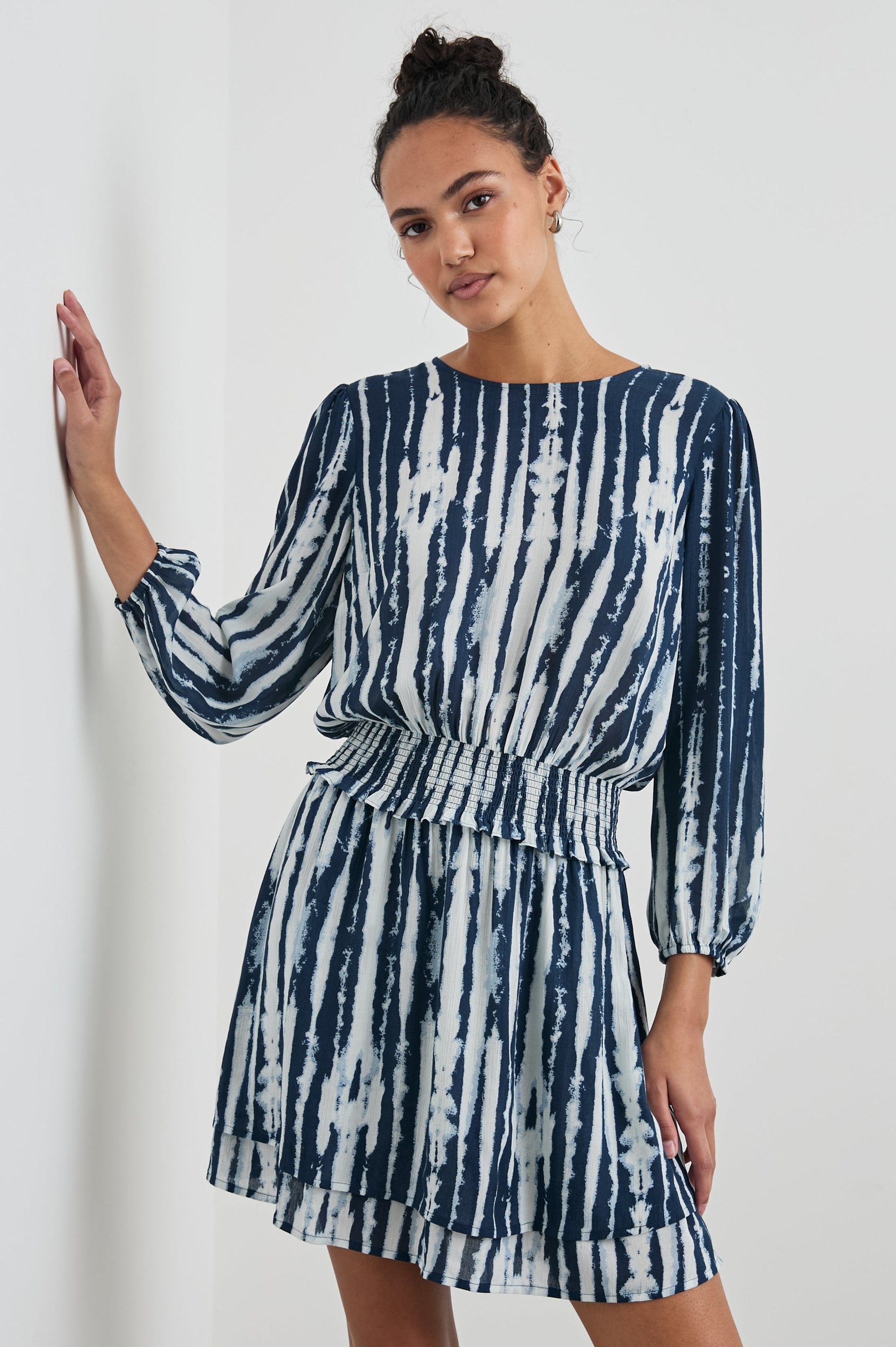 Inez Mini Dress with Three-Quarter Sleeves, a Shallow Scoop Neck, a Smocked Waist, Elasticized Cuffs and a Double Layer Skirt in Indigo Nile Colorway, White and Blue Vertical Streaks - Front View Featured on Model 
