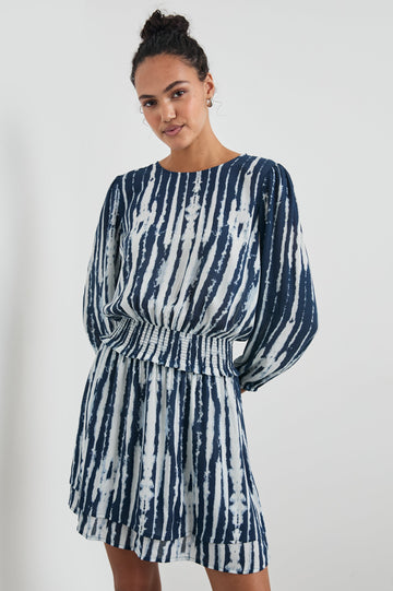 Inez Mini Dress with Three-Quarter Sleeves, a Shallow Scoop Neck, a Smocked Waist, Elasticized Cuffs and a Double Layer Skirt in Indigo Nile Colorway, White and Blue Vertical Streaks - Front View Featured on Model 