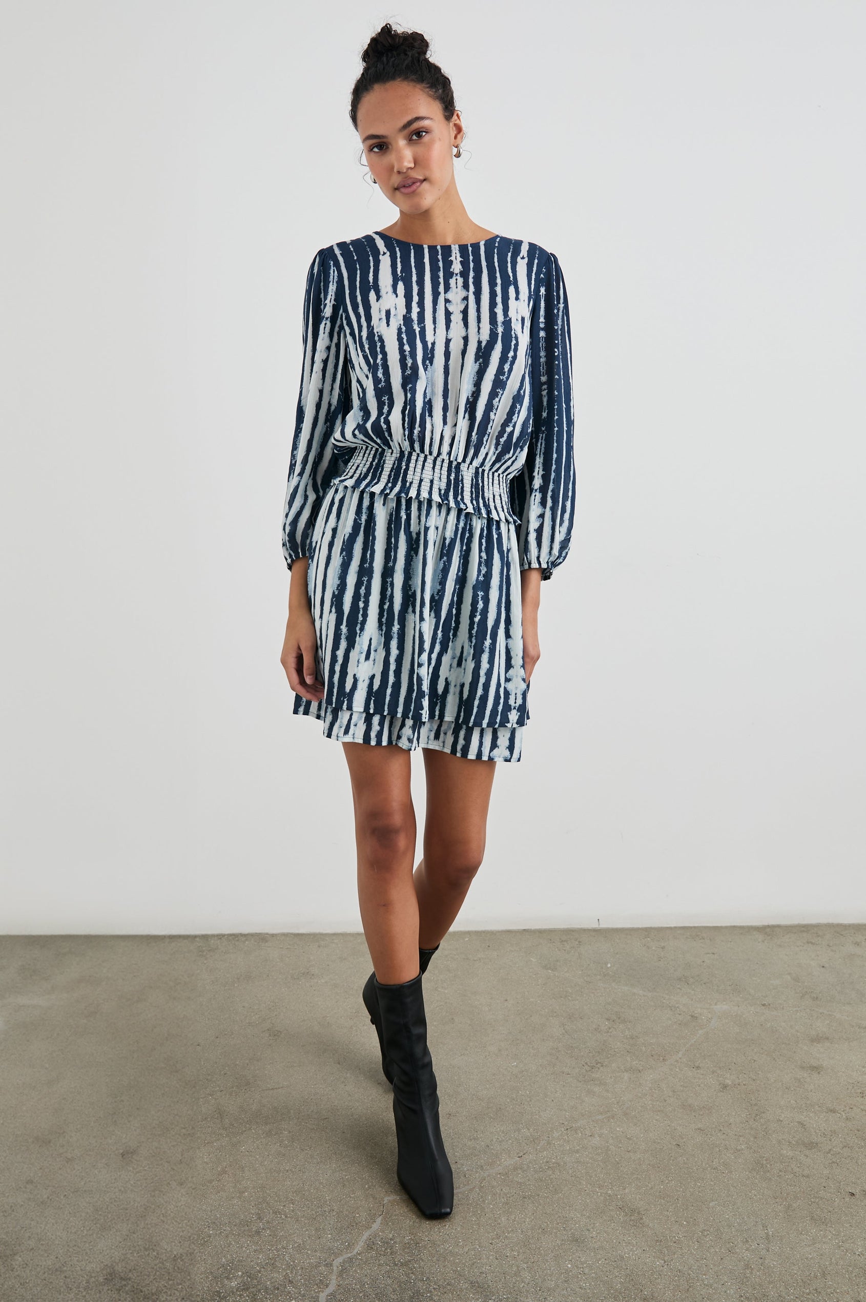 Inez Mini Dress with Three-Quarter Sleeves, a Shallow Scoop Neck, a Smocked Waist, Elasticized Cuffs and a Double Layer Skirt in Indigo Nile Colorway, White and Blue Vertical Streaks - Front Full Body View Featured on Model 