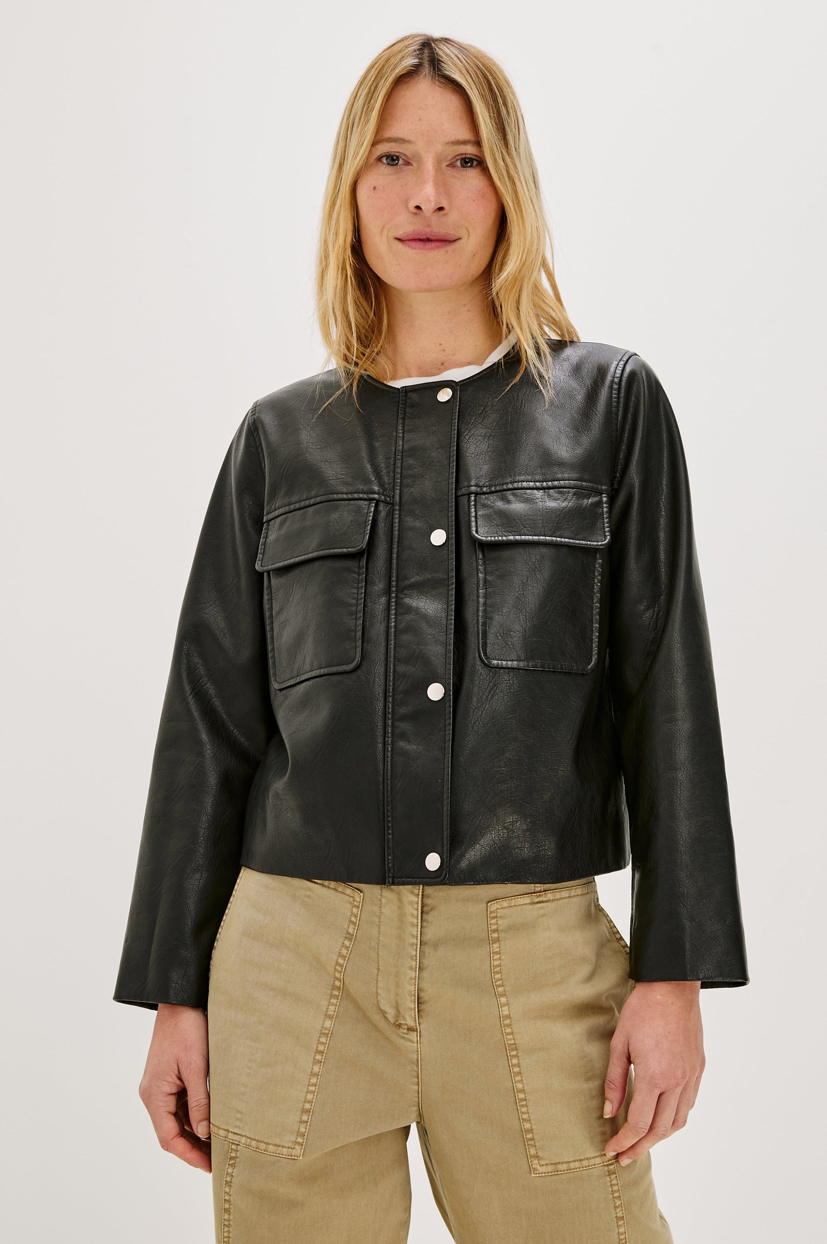 Inka, a cropped, boxy faux leather jacket in a black, slightly distressed finish. The design includes classic chest pockets and a structured silhouette. Front View featured on model, Buttoned