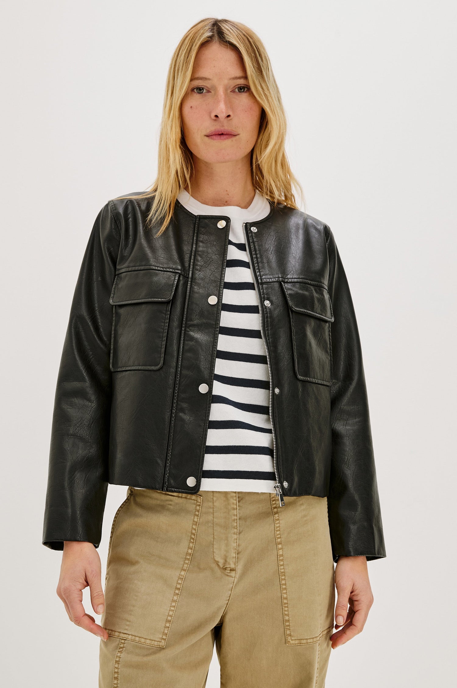 Inka, a cropped, boxy faux leather jacket in a black, slightly distressed finish. The design includes classic chest pockets and a structured silhouette. Front View featured on model, Unzipped