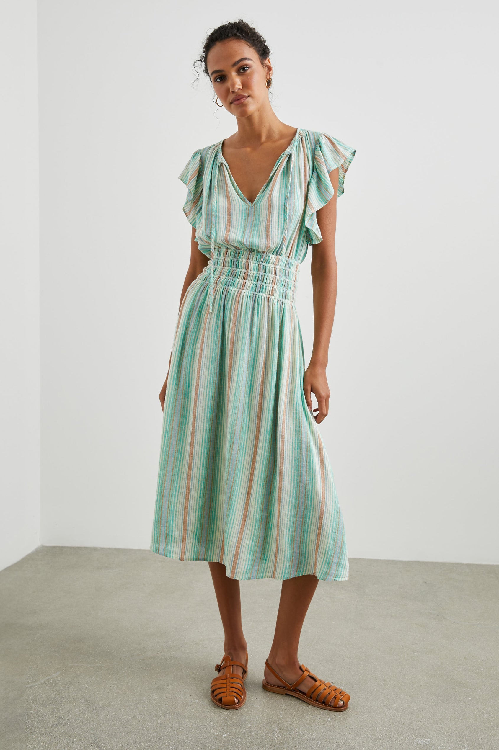 Iona Short Sleeve Midi Dress with Flutter Sleeves, a Deep V Neck with Ties, and a Shirred Waist in Seaview Stripe Colorway, Vertical Stripes in Browns, Blues and Creams - Front Full Body View Featured on Model 