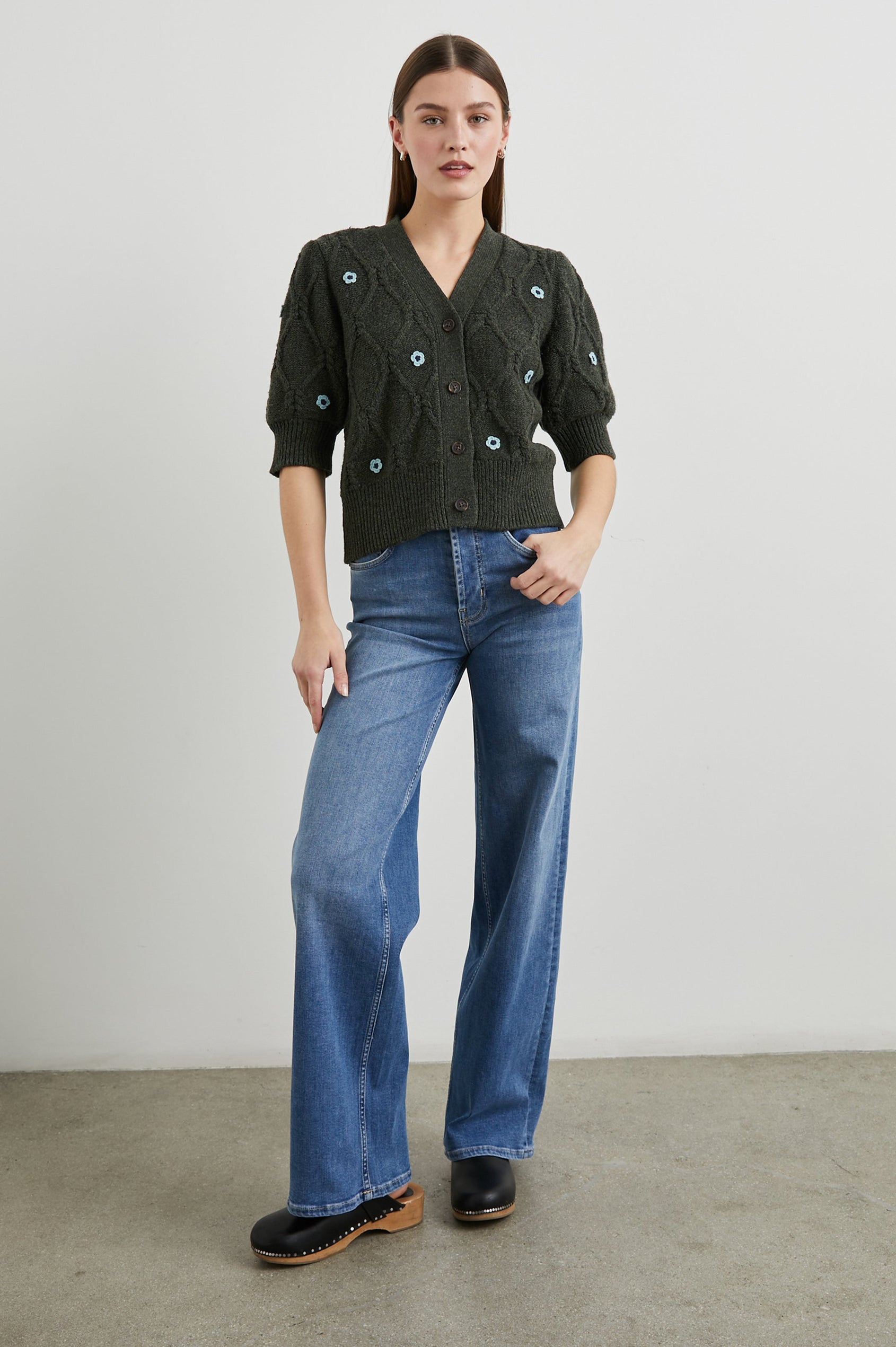 Isla Mid-length-Sleeve Cardigan with Ribbed Hems and Cuffs and Button Closure in Forest Daisies Colorway, with blue crochet daisies on forest green - Front Full Body View Featured on Model