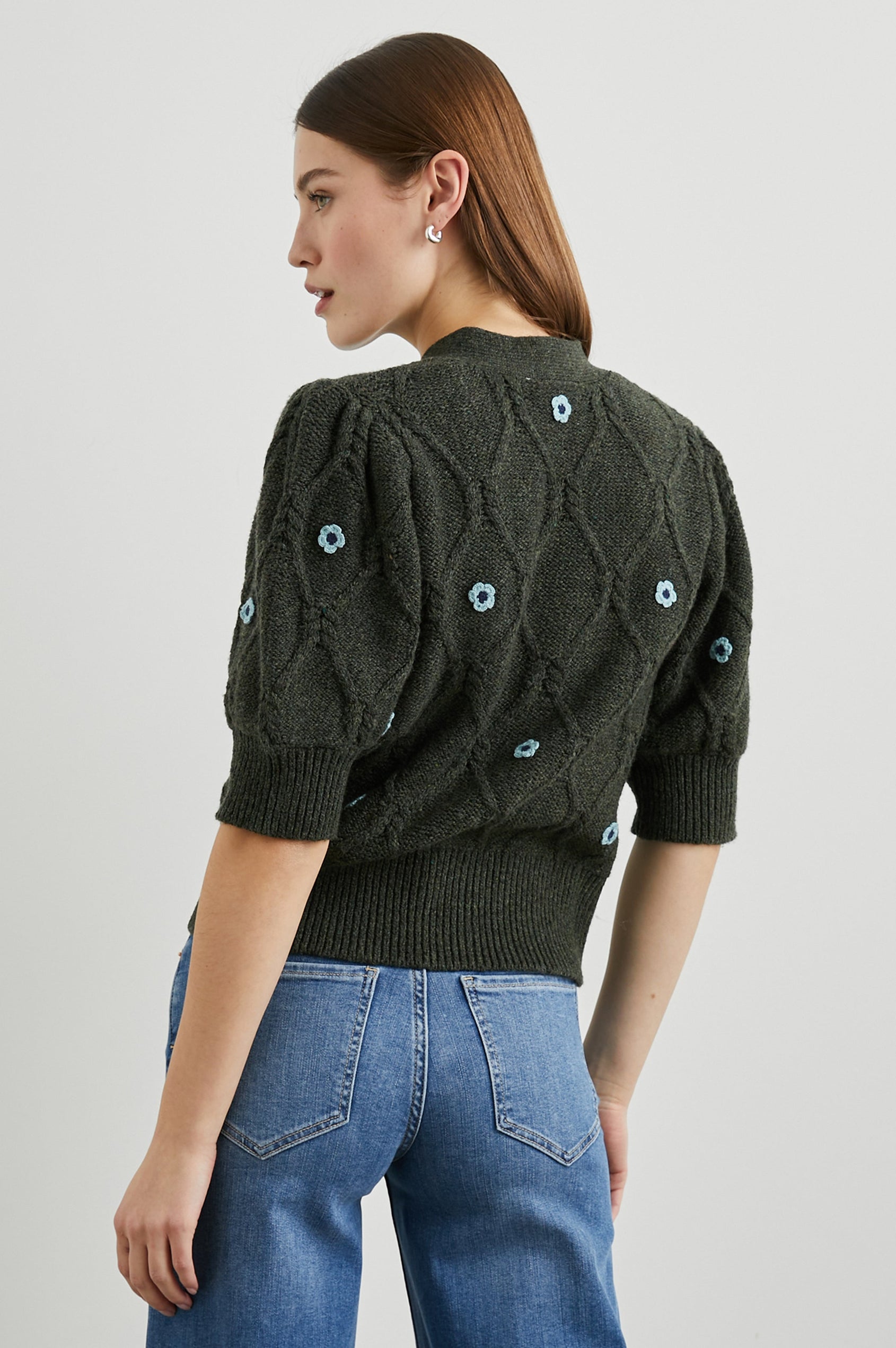 Isla Mid-length-Sleeve Cardigan with Ribbed Hems and Cuffs and Button Closure in Forest Daisies Colorway, with blue crochet daisies on forest green - Back View Featured on Model
