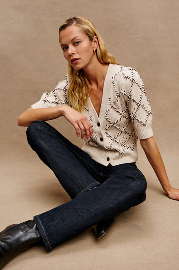 The Isla is a half sleeve cardigan, v-neck and button front with cross hatch rope applique and rib trim in Oat colorway. Front view featured on model.