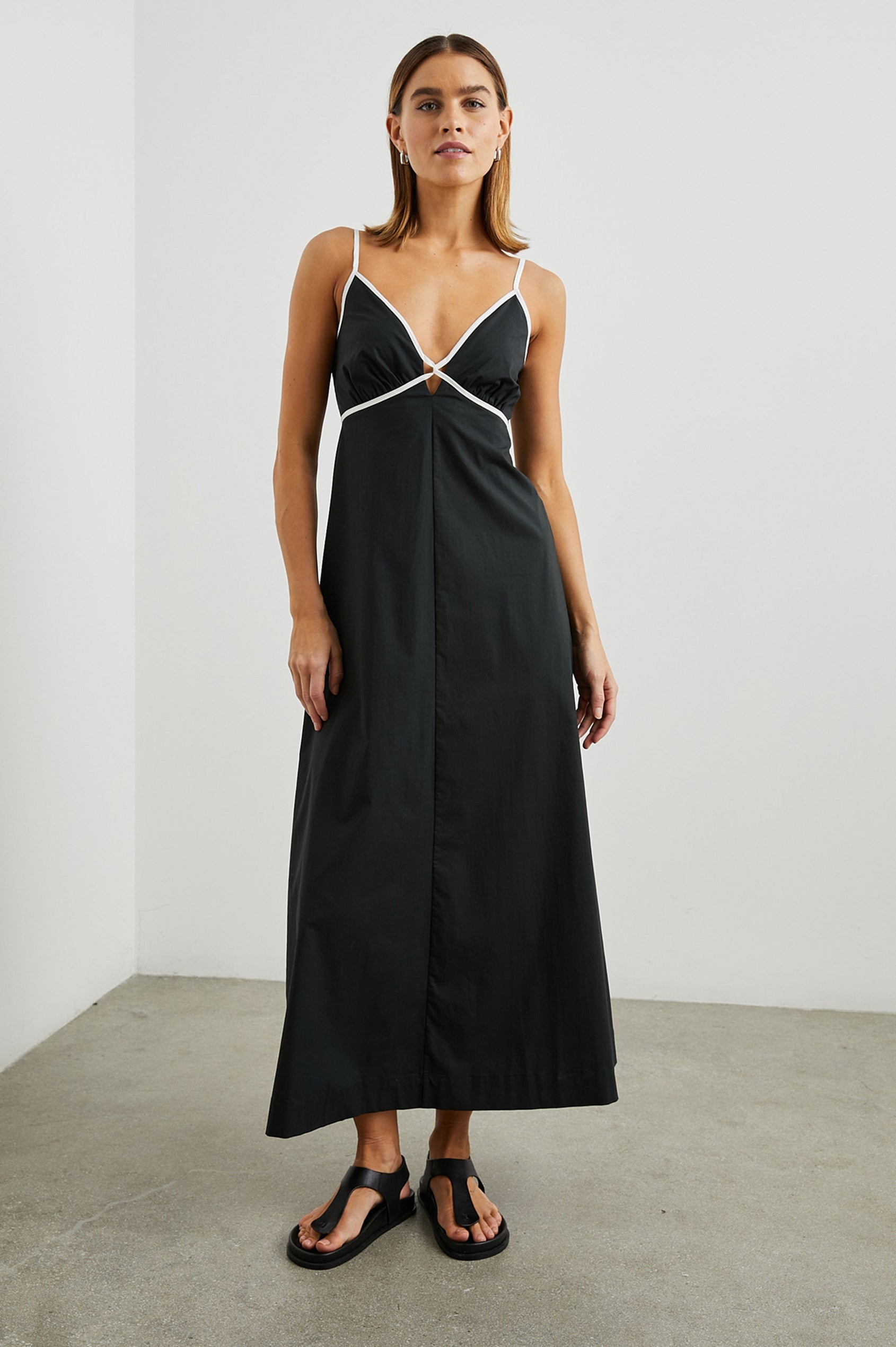 Jessa Sleeveless Maxi Dress with Adjustable Spaghetti Straps, a Deep V Neck with a Cutout, a Shirred Back and White Trim on the Bodice in Black Colorway - Front Full Body View Featured on Model 