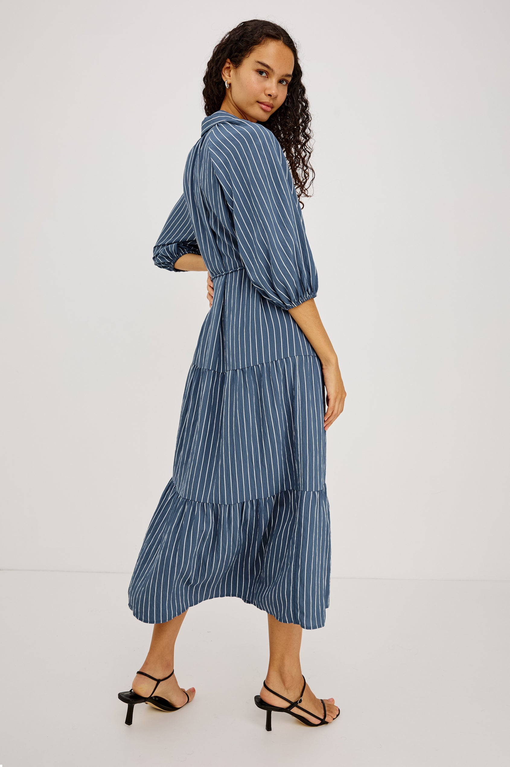 June Maxi Dress in Soft Crinkle Shirting With Three-Quarter Puff Sleeves, Point Collar, Full Front Button Placket, and Self-Tie Waist in Washed Indigo Stripe Colorway - Lower Body Back View Featured on Model