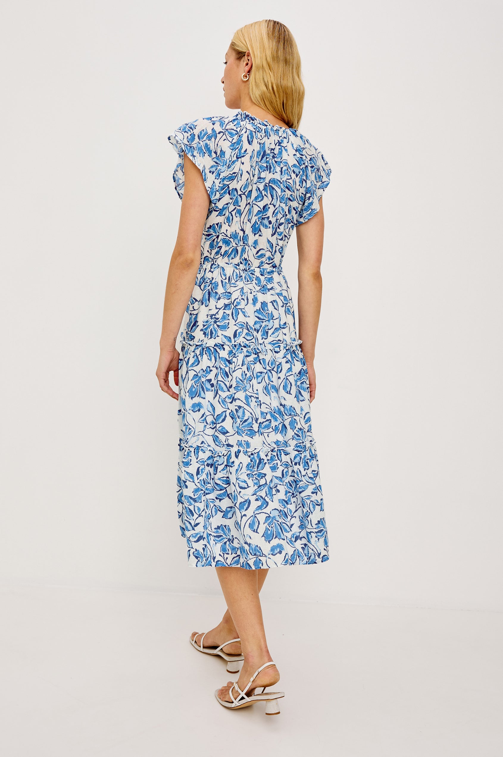 Juni Maxi in Linen With Ruffled Split V-Neckline Flutter Sleeves Adjustable Waist Ties and Fully Lined Tiered Skirt in Azure Jasmine Colorway - Full Body Back View Featured on Model
