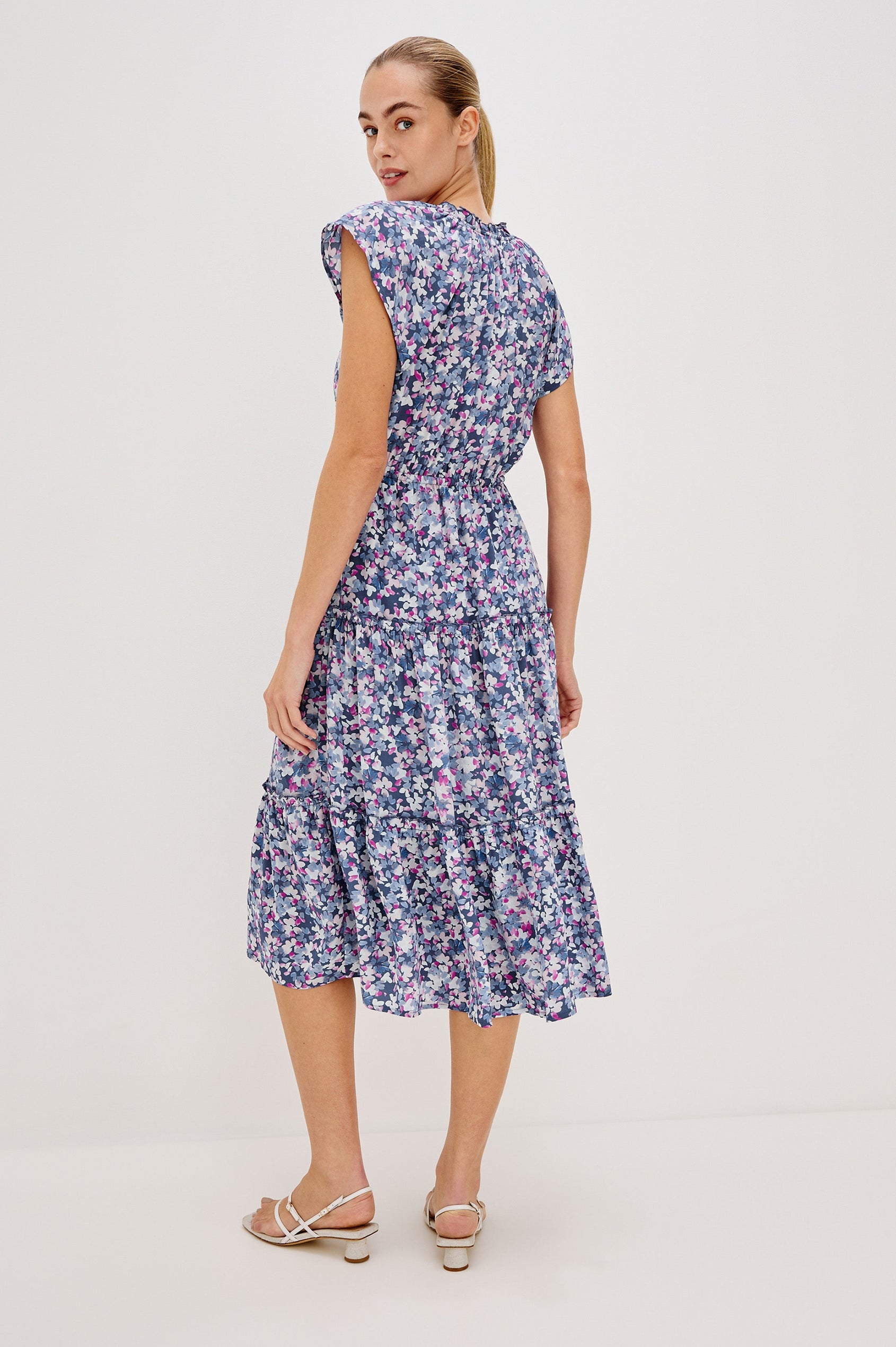 Juni Tiered Midi Dress with a V-Neck, Ruffled Neckline, Short Flutter Sleeves, Drawstring Waist Detail in Blue Blossom Colorway. Full Body Back View Shown on Model. 
