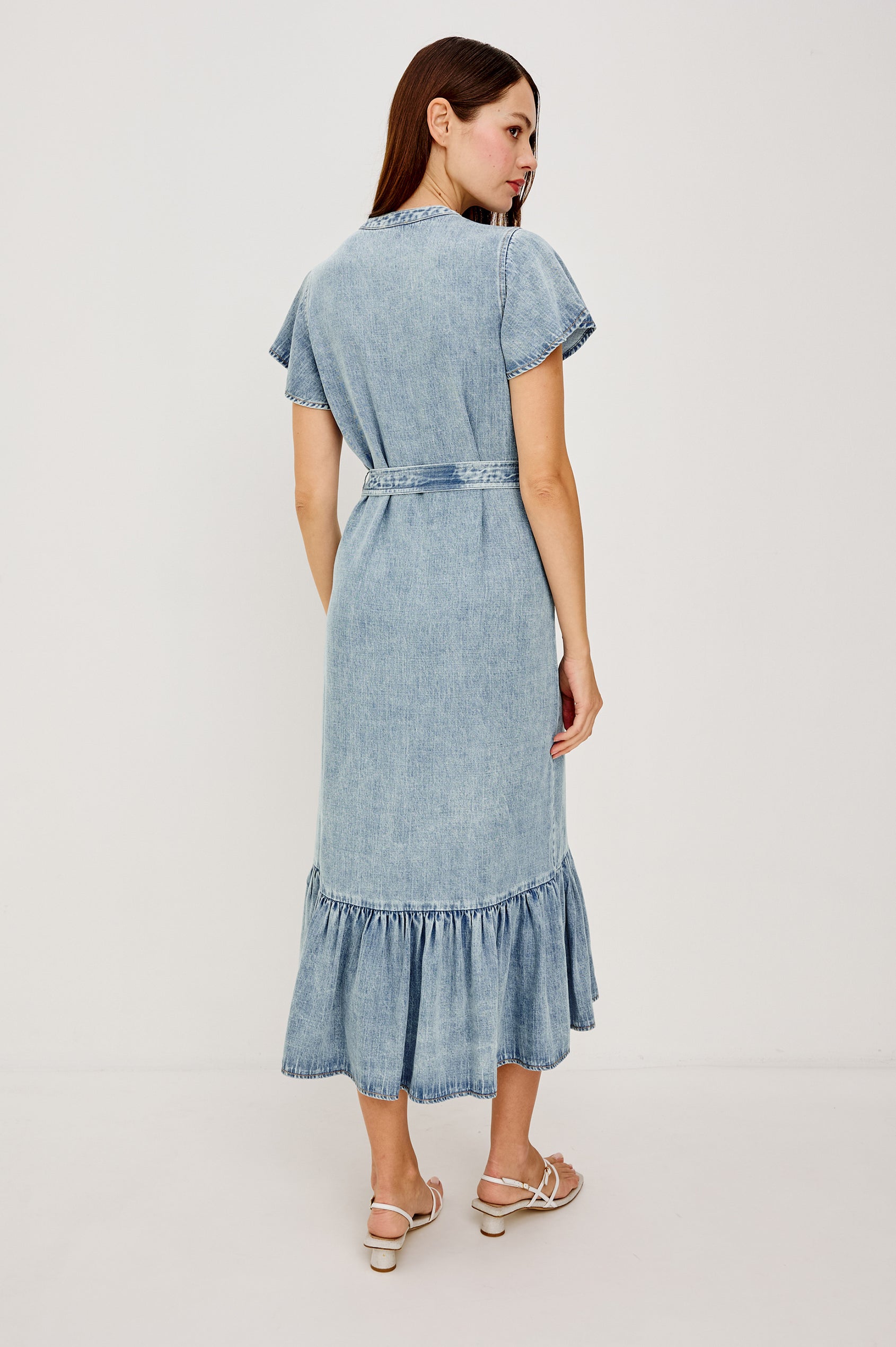 Kahlo TENCELâ„¢ Denim Shirt Dress With Short Flutter Sleeves Front Buttons a Single Chest Patch Pocket Adjustable Belted Ties Ruffle Hem in Faded Indigo Colorway - Full Body Back View Featured on Model