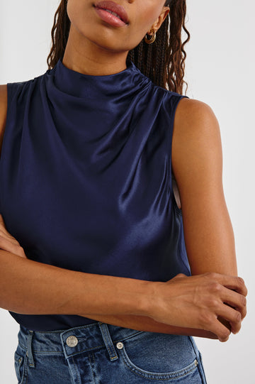 Kaleen Sleeveless Top with Mock Neck with Buttons and Keyhole on the Back and Draped Fabric on the Upper Chest in Navy Colorway - Front Tucked View Featured on Model
