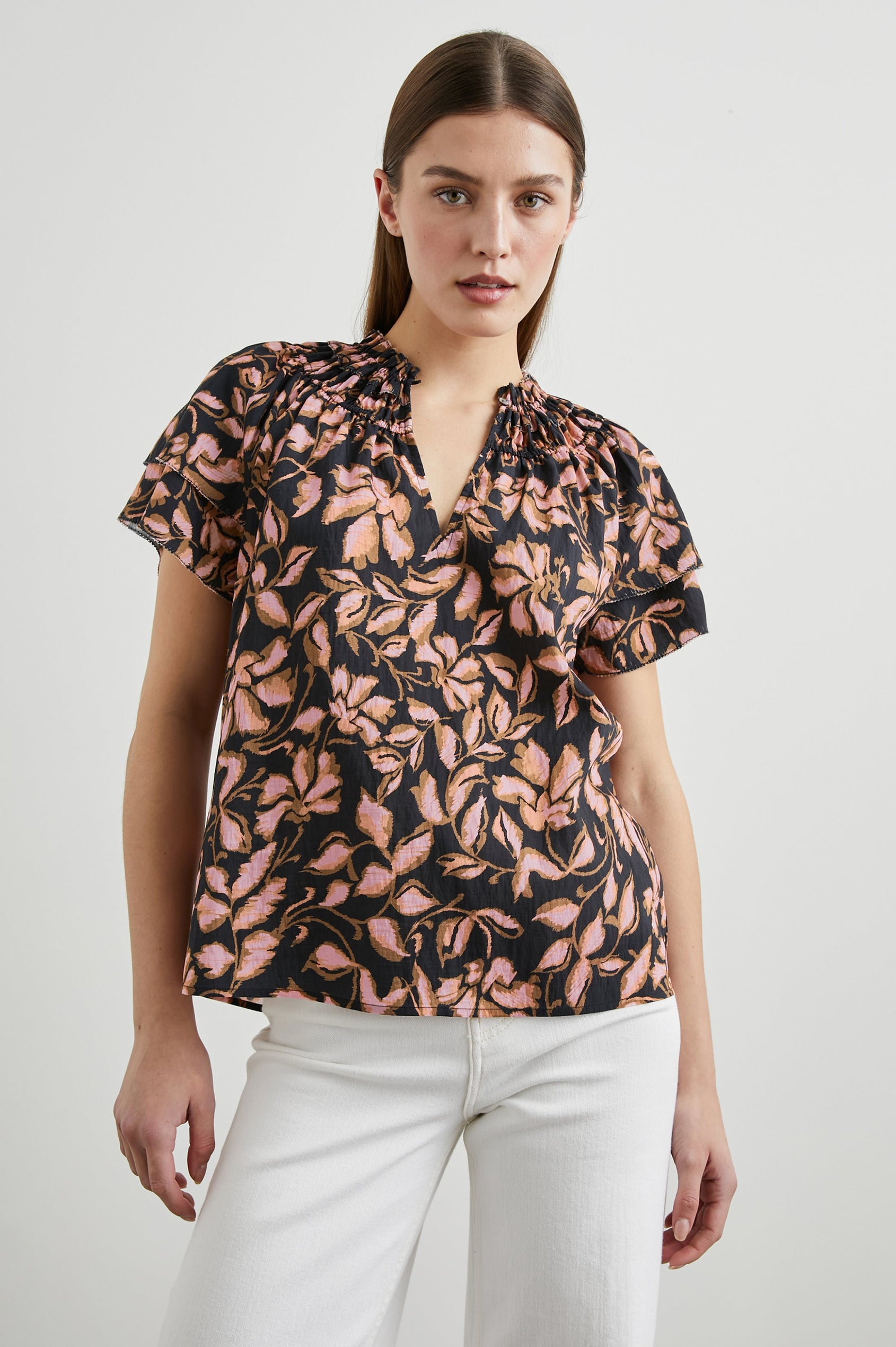 Kamila Short-Sleeve Top with Ruffled Sleeves, Deep V neck, and a Shirred Collar with a button in Jasmine Colorway, with pink and brown flowers on black - Front Tucked View Featured on Model