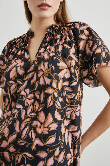 Kamila Short-Sleeve Top with Ruffled Sleeves, Deep V neck, and a Shirred Collar with a button in Jasmine Colorway, with pink and brown flowers on black - Front View Featured on Model